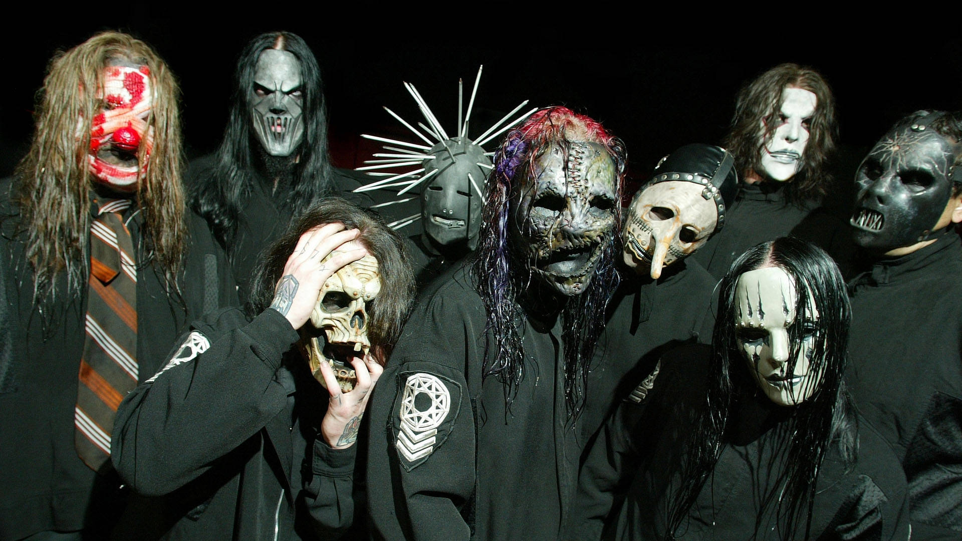Slipknot 桌布 壁紙 — 一群恐怖主題的音樂家，戴著怪誕的面具和穿著深色衣服，在黑色背景下強烈地擺姿勢。