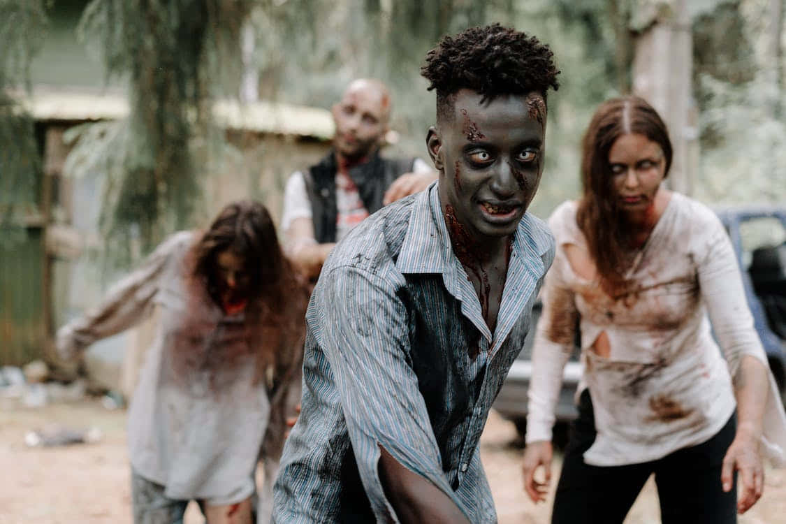Scary Zombie 桌布 壁紙 — 一群恐怖的殭屍，臉上沾滿血跡，衣衫襤褸，在破敗的戶外環境中蹣跚前行。
