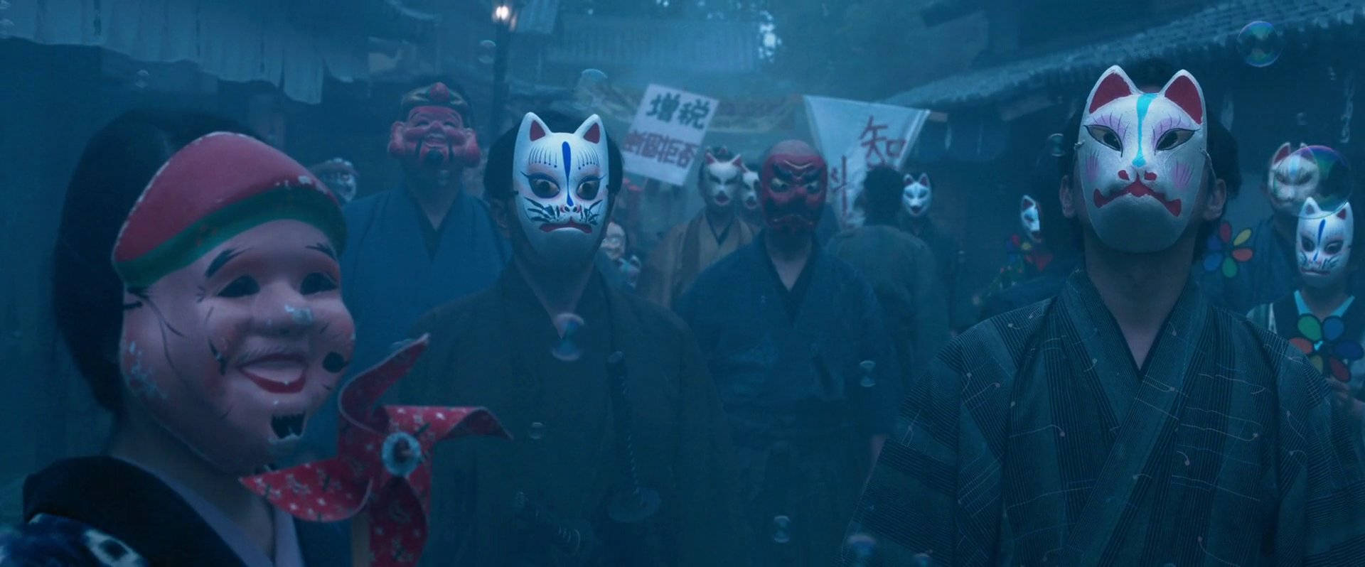 prisoners of the ghostland 桌布 壁紙 — 一群戴著傳統日本節日面具的人站在霧氣瀰漫的夜晚街道上，昏暗的燈籠下。