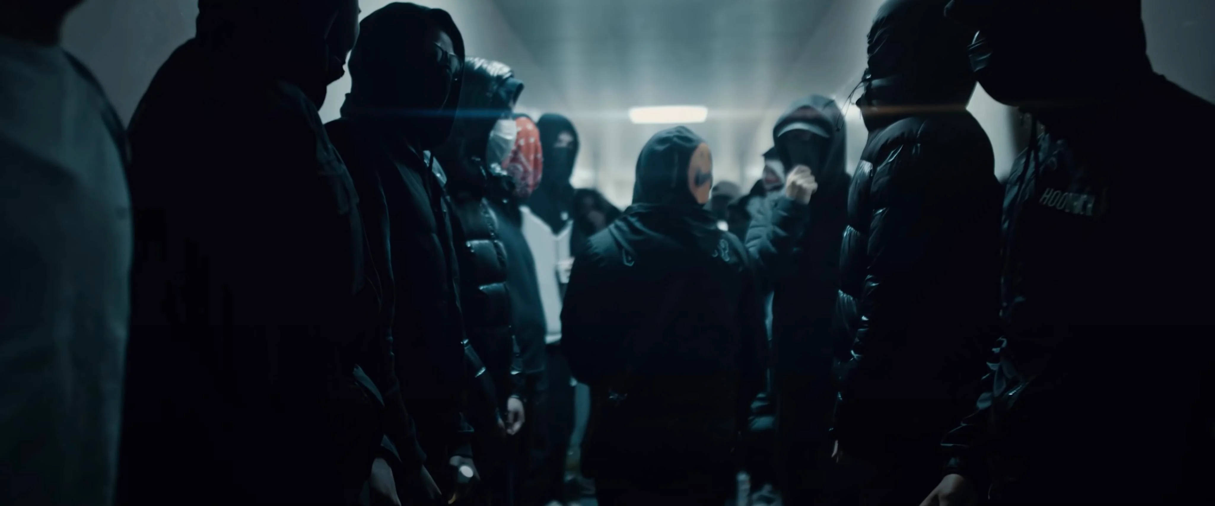 Rappers 桌布 壁紙 — 一群戴著兜帽的神秘人物站在光線昏暗的隧道中，頭頂上一盞燈投射出刺眼的光束。
