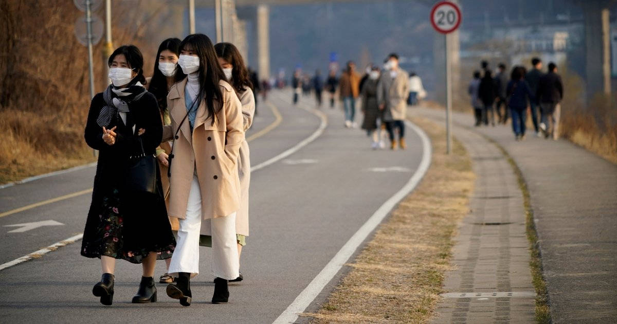 Coronavirus 桌布 壁紙 — 一群戴著口罩的女性沿著彎曲的鋪砌小徑行走，遠處有其他行人，天空朦朧。