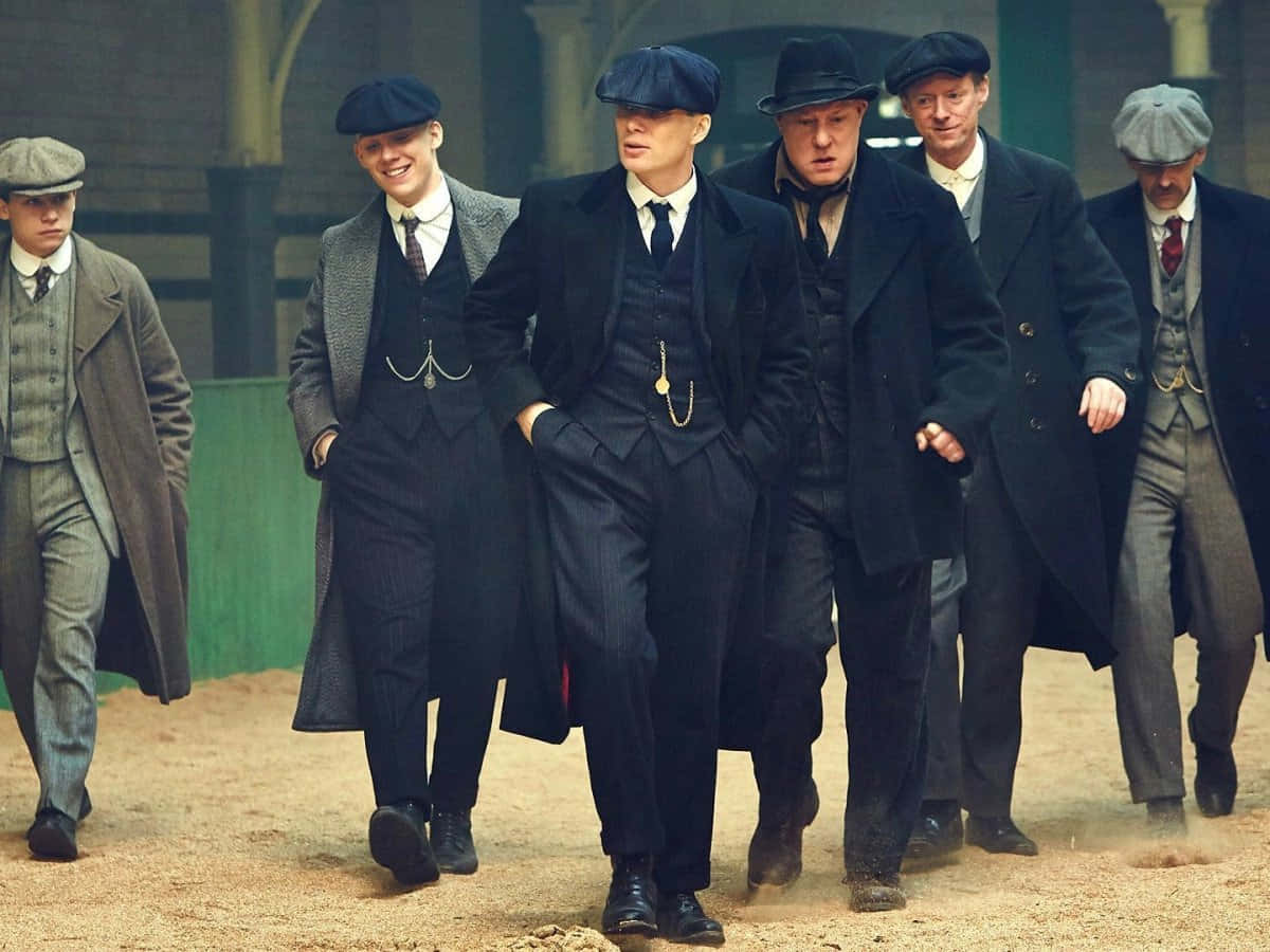 戴著復古平頂帽和穿著大衣的男人在塵土飛揚的小徑上行走。 — Peaky Blinders 壁紙