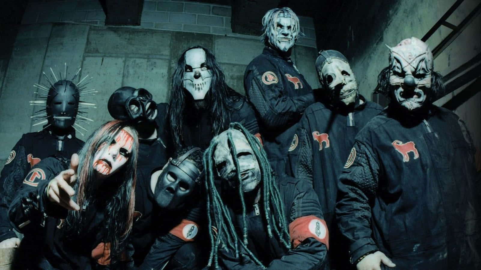 Slipknot 桌布 壁紙 — 一群戴著面具、身穿深色制服的音樂人在粗糙的混凝土走廊中強烈地擺姿勢。