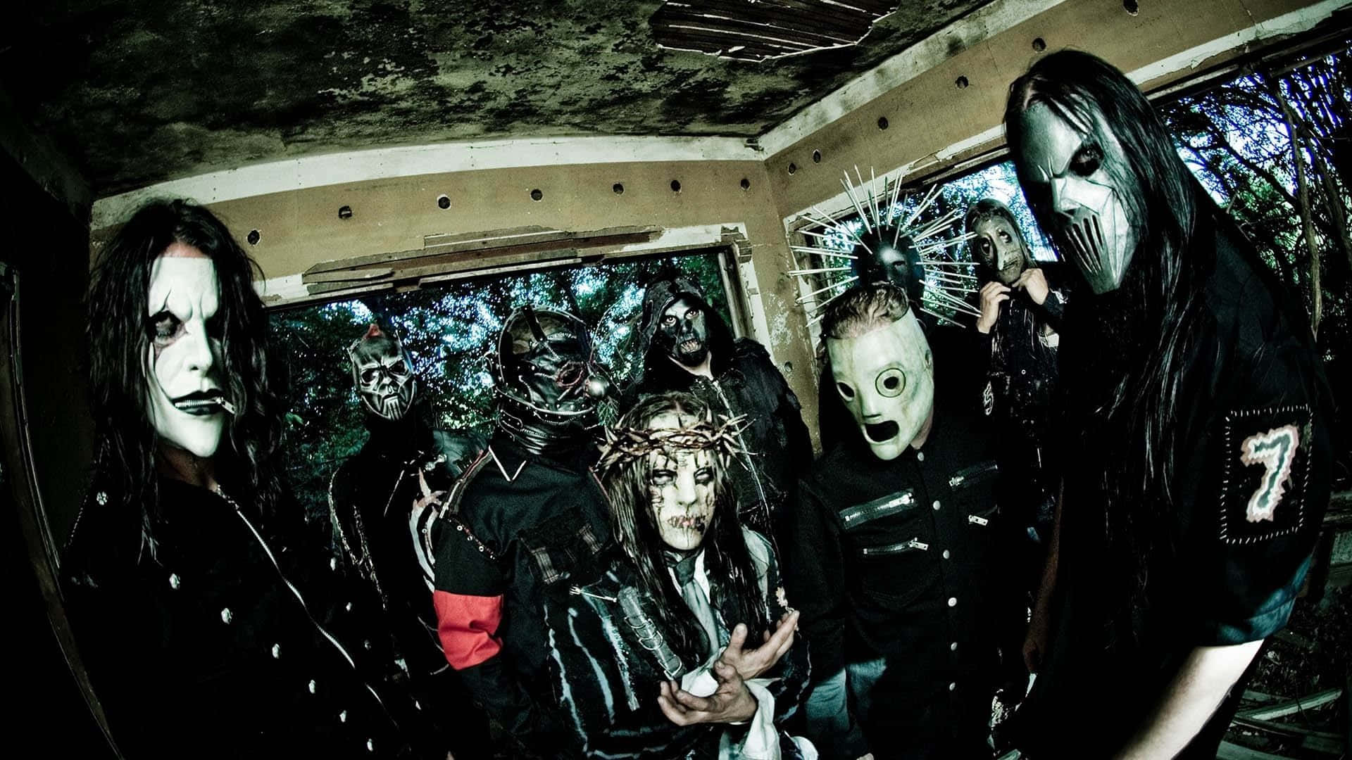 Slipknot 桌布 壁紙 — 一群戴著面具、身穿黑色服裝的音樂人在一個佈滿青苔、窗戶破損的破舊房間內擺出威脅姿勢。