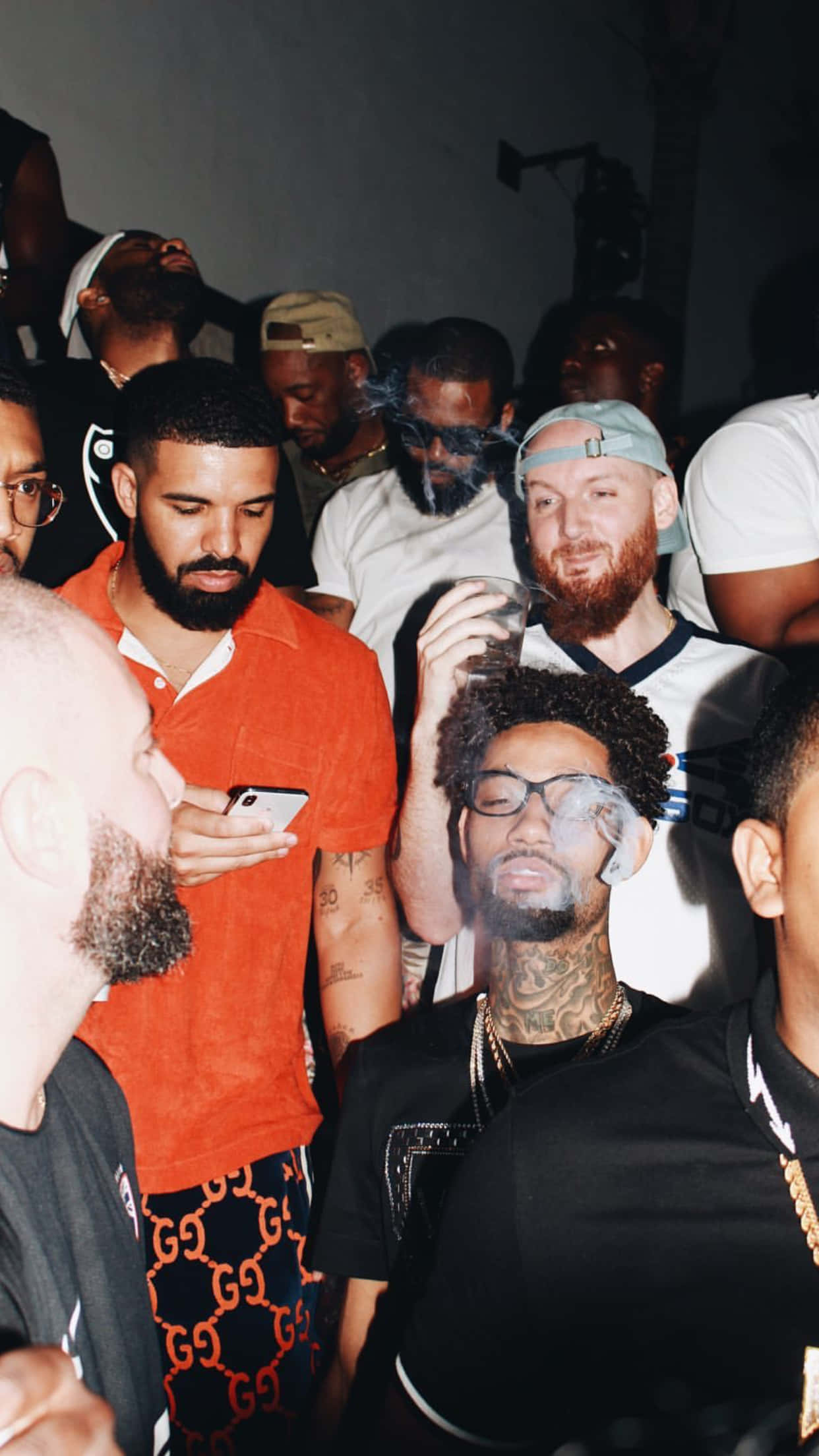 Aesthetic Drake 桌布 壁紙 — 一群時尚男士在派對中，燈光昏暗，煙霧在臉龐縈繞，紋身在低光下可見。