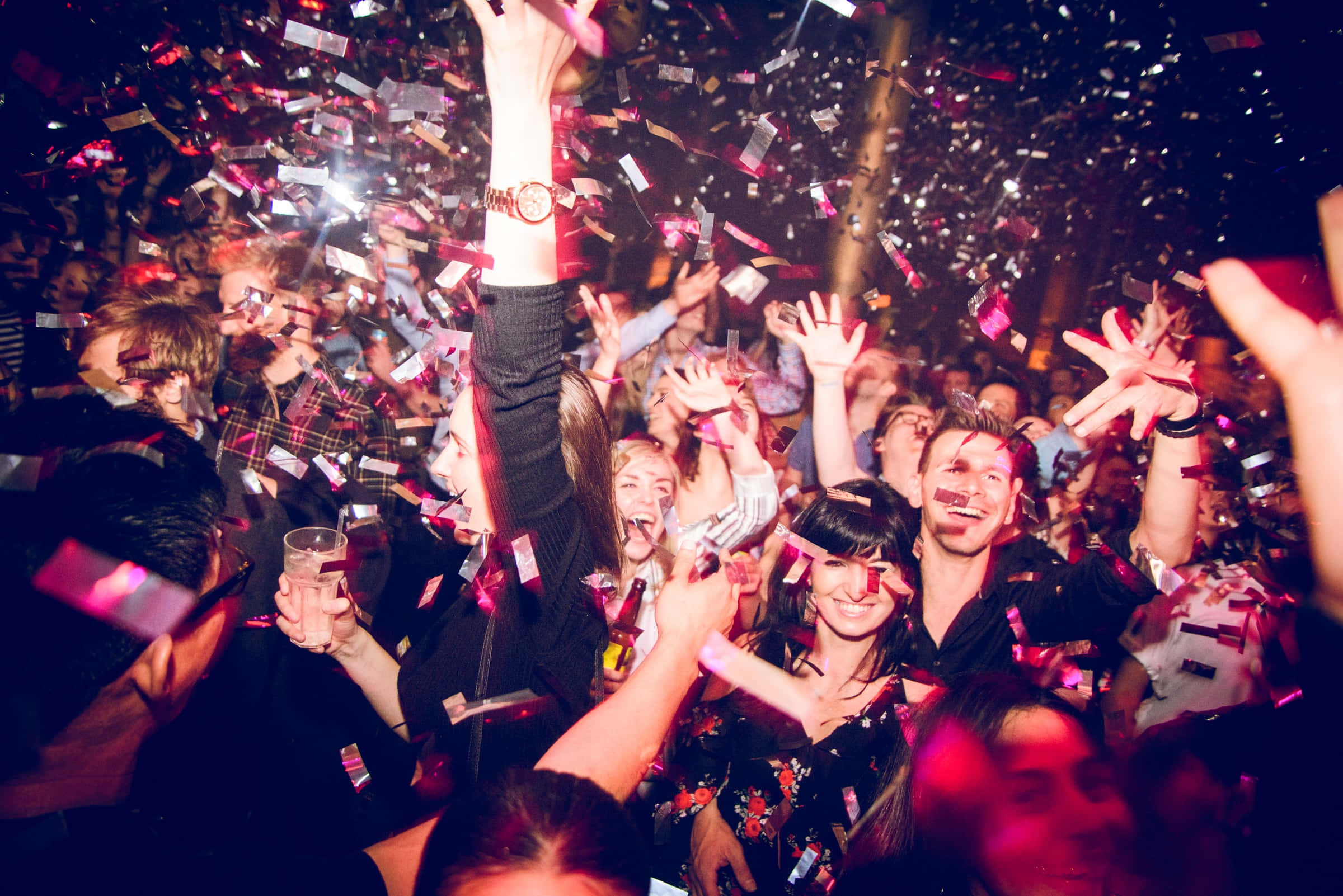 Party 桌布 壁紙 — 一群歡樂的派對參與者在充滿活力的夜總會中，於飄落的粉紅色和銀色五彩紙屑下慶祝。