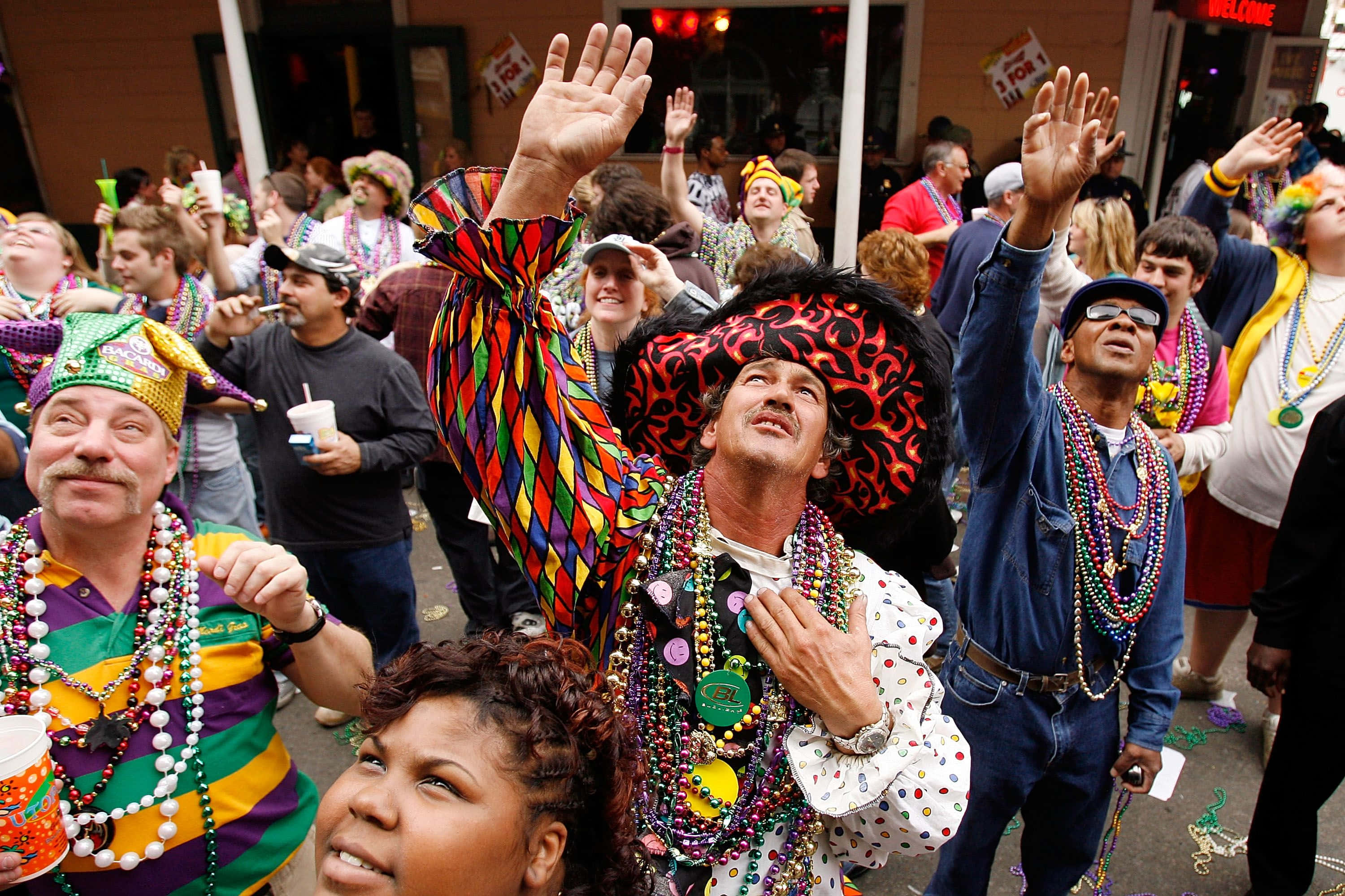 Mardi Gras 桌布 壁紙 — 一群歡樂的狂歡者穿著色彩繽紛的Mardi Gras服裝和珠子在熱鬧的街道上跳舞。