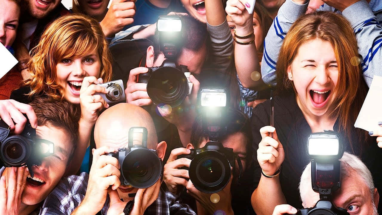 Paparazzi 桌布 壁紙 — 一群混亂的興奮攝影師，閃光燈閃爍，在充滿活力的日光下捕捉瞬間。