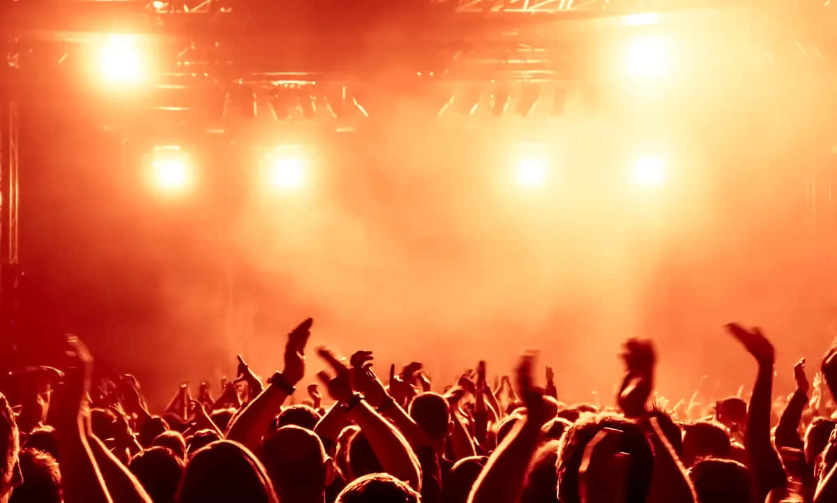 concert 桌布 壁紙 — 一群演唱會觀眾在煙霧瀰漫的橙色舞台燈光下舉起雙手。