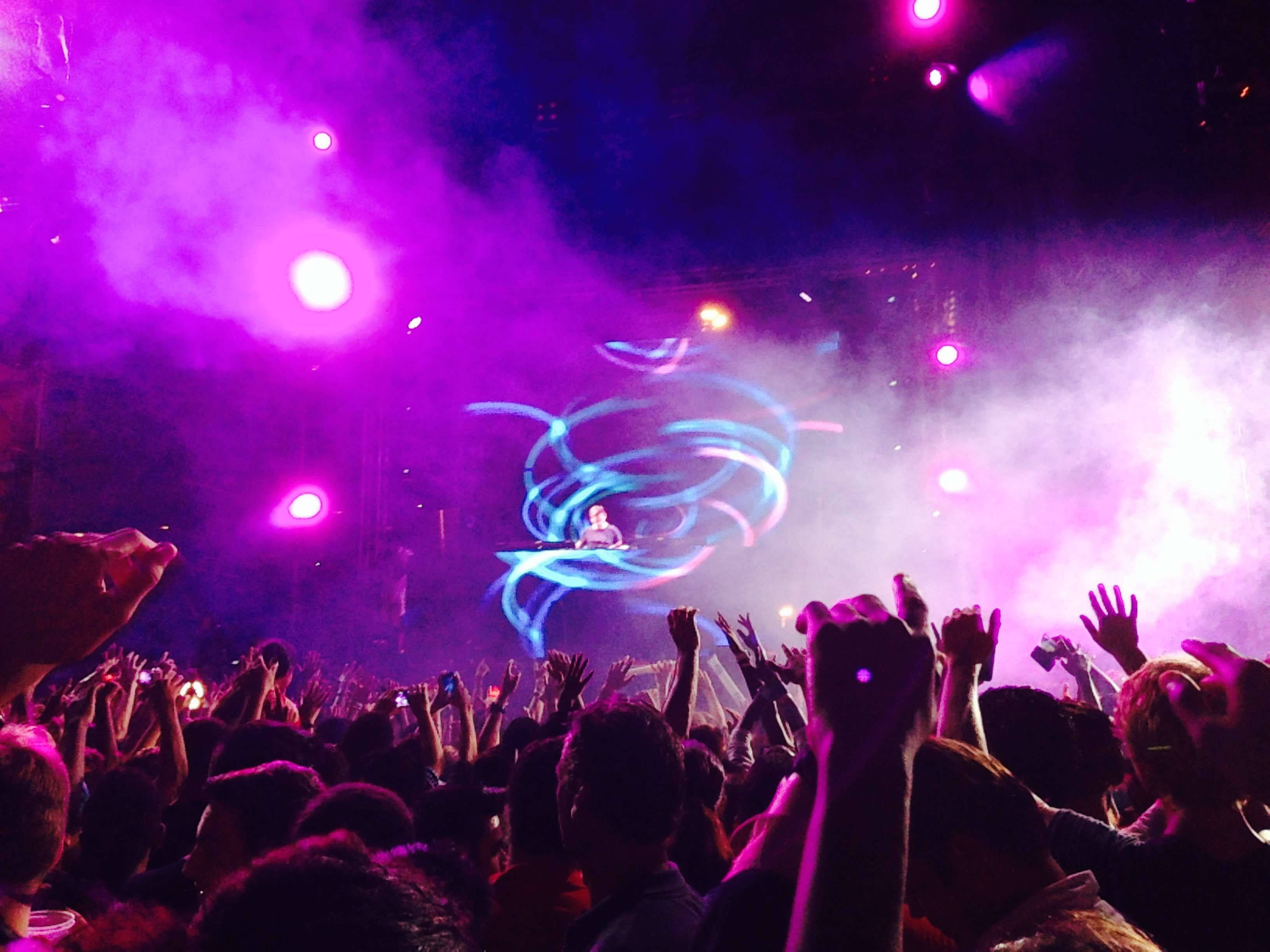 Party 桌布 壁紙 — 一群演唱會觀眾在紫色燈光下舉起雙手，表演者在舞台上演奏，伴隨著旋轉的藍色雷射燈光。