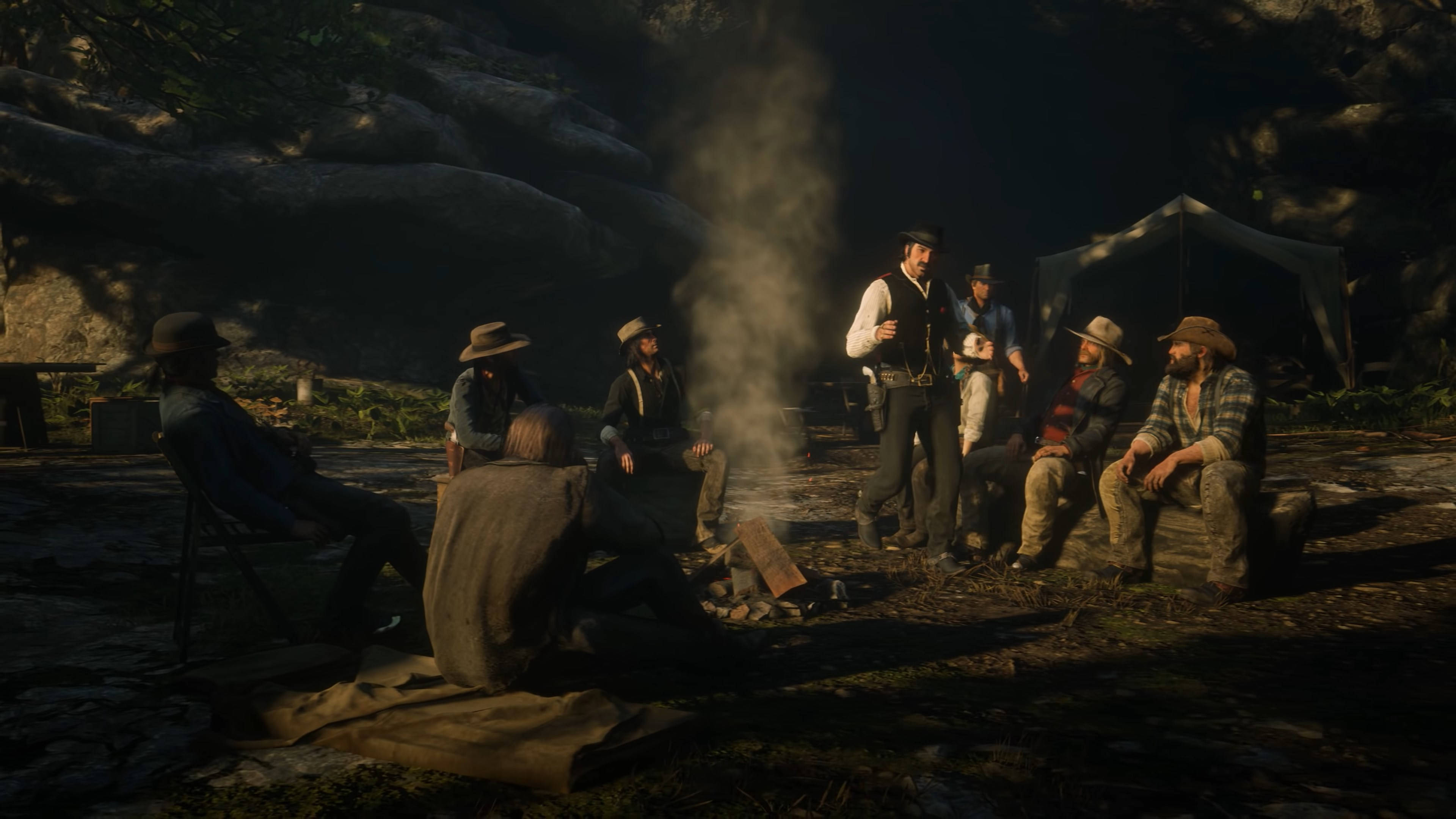 Red Dead Redemption 2 Desktop 桌布 壁紙 — 一群牛仔在溫暖的金色光芒下，聚集在岩石荒野中冒煙的營火周圍。
