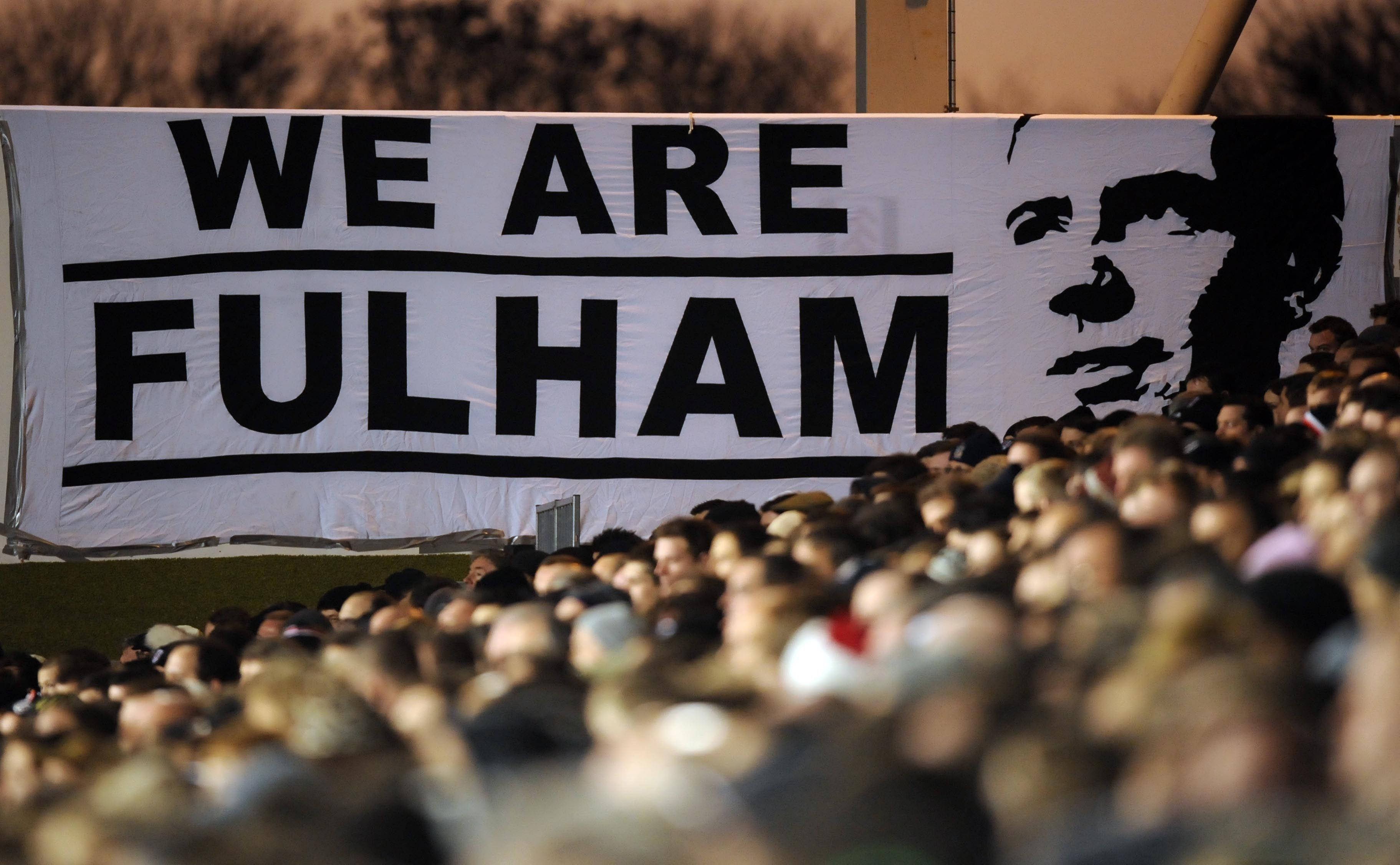 Cheering 桌布 壁紙 — 一群球迷舉著一個大型橫幅，上面寫著WE ARE FULHAM，並有一個黑色男性面孔剪影，背景是模糊的體育場。