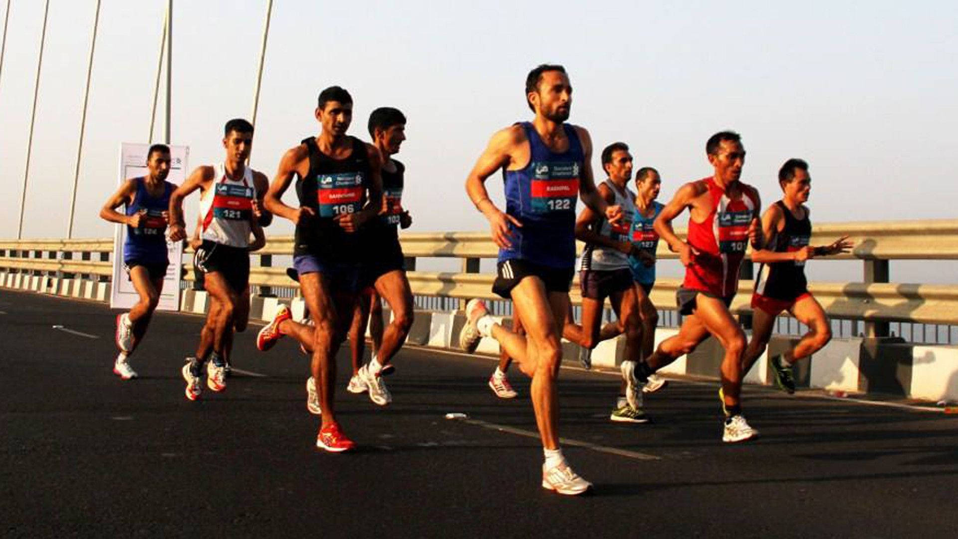 Marathon 桌布 壁紙 — 一群男性跑者在黃金時段於寬闊的橋上比賽，長長的影子在他們身後延伸。