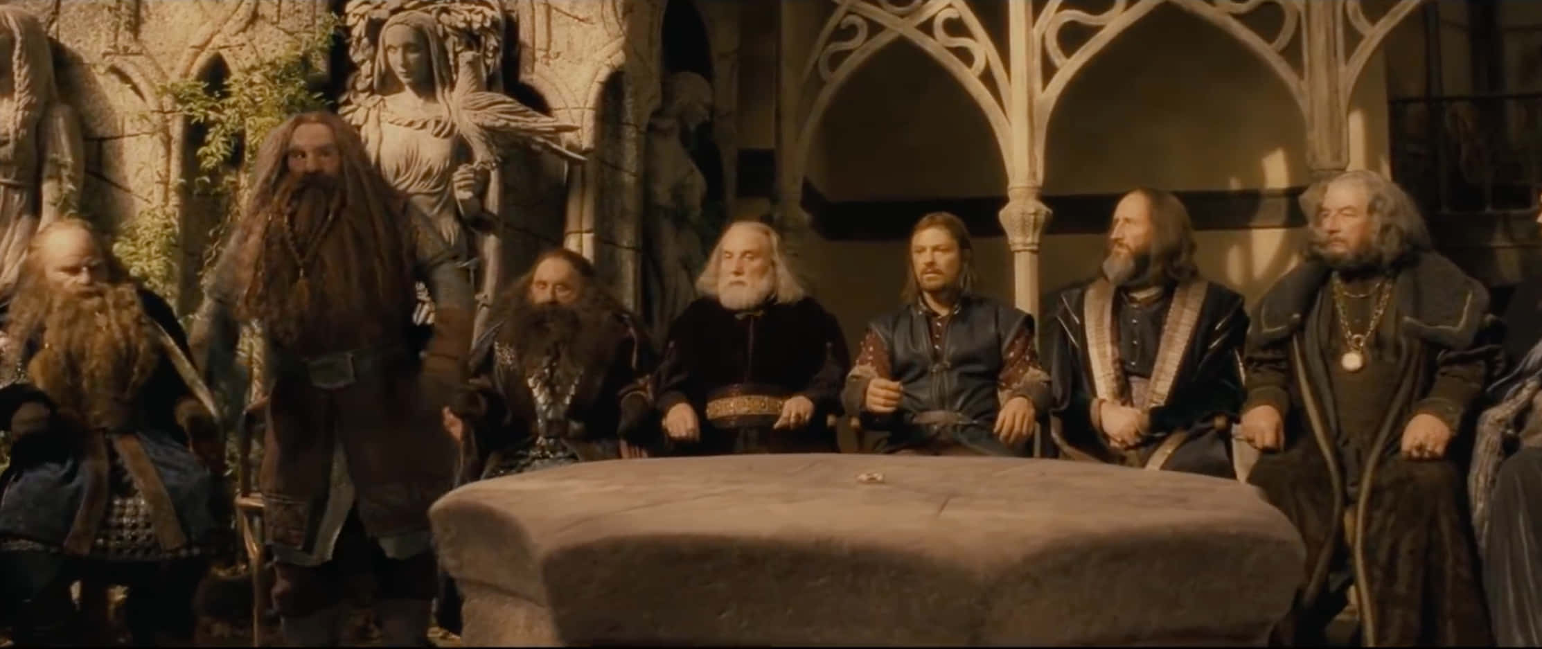 Lord Of The Rings Zoom 桌布 壁紙 — 一群留鬍鬚的矮人穿著中世紀風格盔甲，坐在哥德式大廳內的石桌旁，大廳有雕像和拱形窗戶。