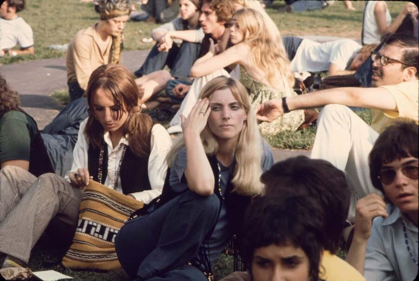 woodstock 桌布 壁紙 — 一群穿著1970年代嬉皮服裝的年輕人坐在草地上，在明亮的陽光下休息。