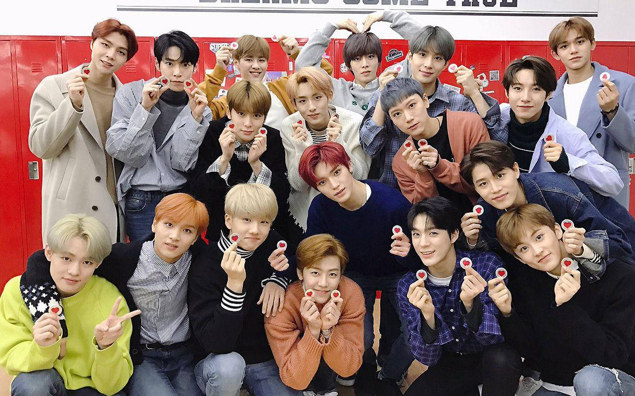 Nct 桌布 壁紙 — 一群穿著休閒服的年輕男子在紅色置物櫃前開心擺姿勢，手持心形糖果。