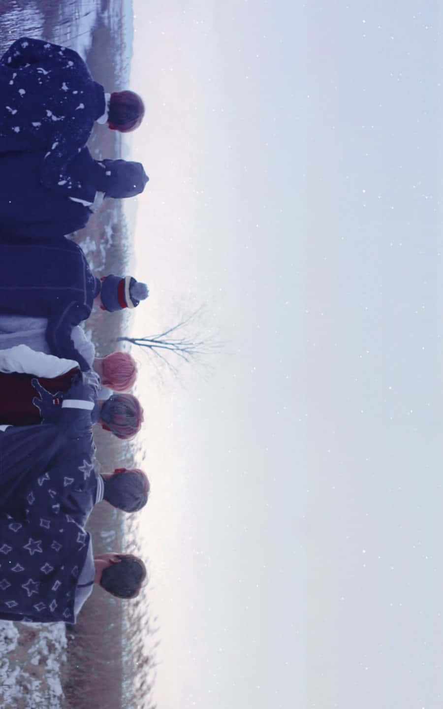 Bts Mv 桌布 壁紙 — 一群穿著冬季外套的人站在雪地裡，望著飄雪的天空。
