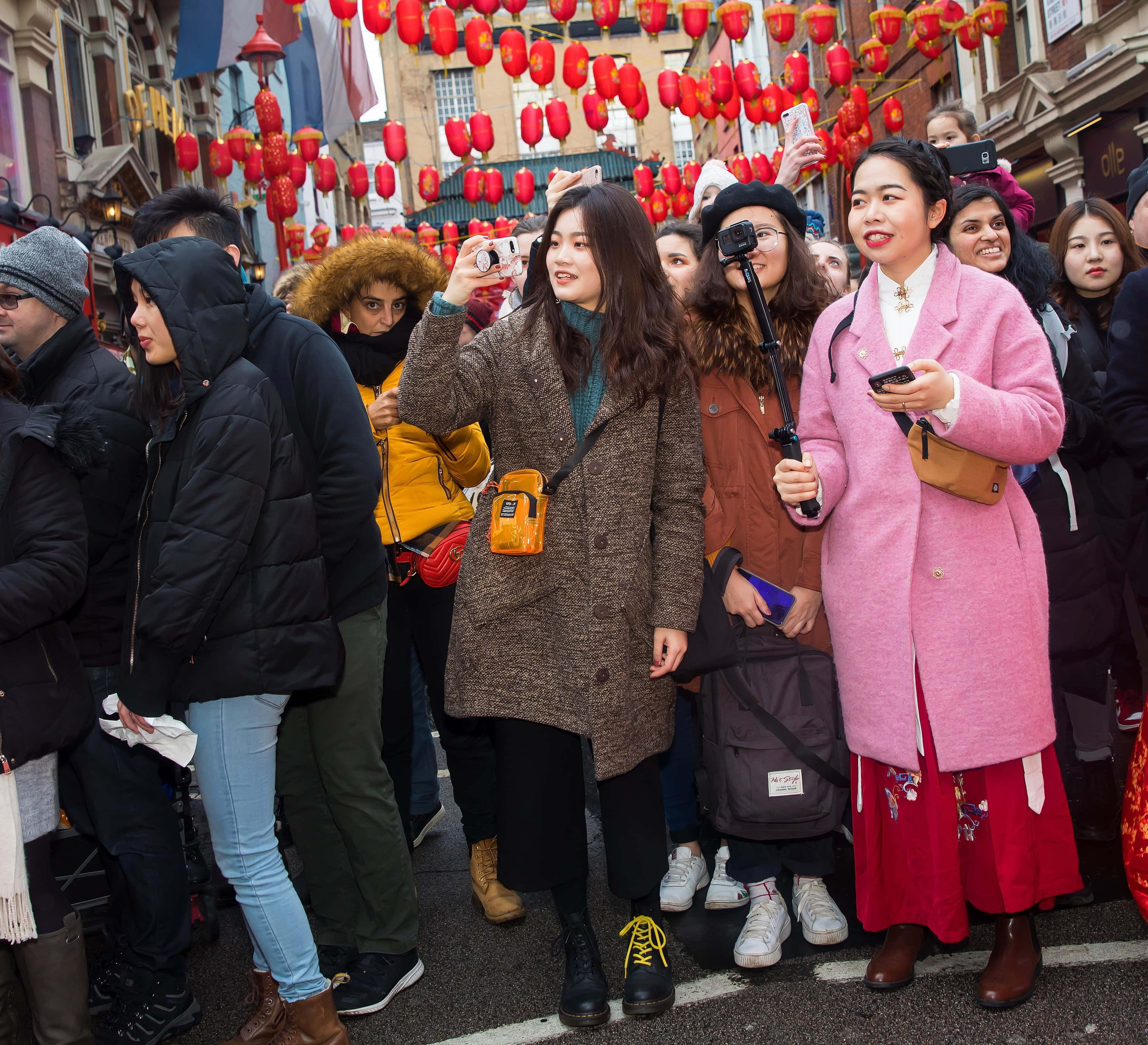 春節 桌布 壁紙 — 一群穿著冬季外套的人群在節日城市街道的紅燈籠下拍照。