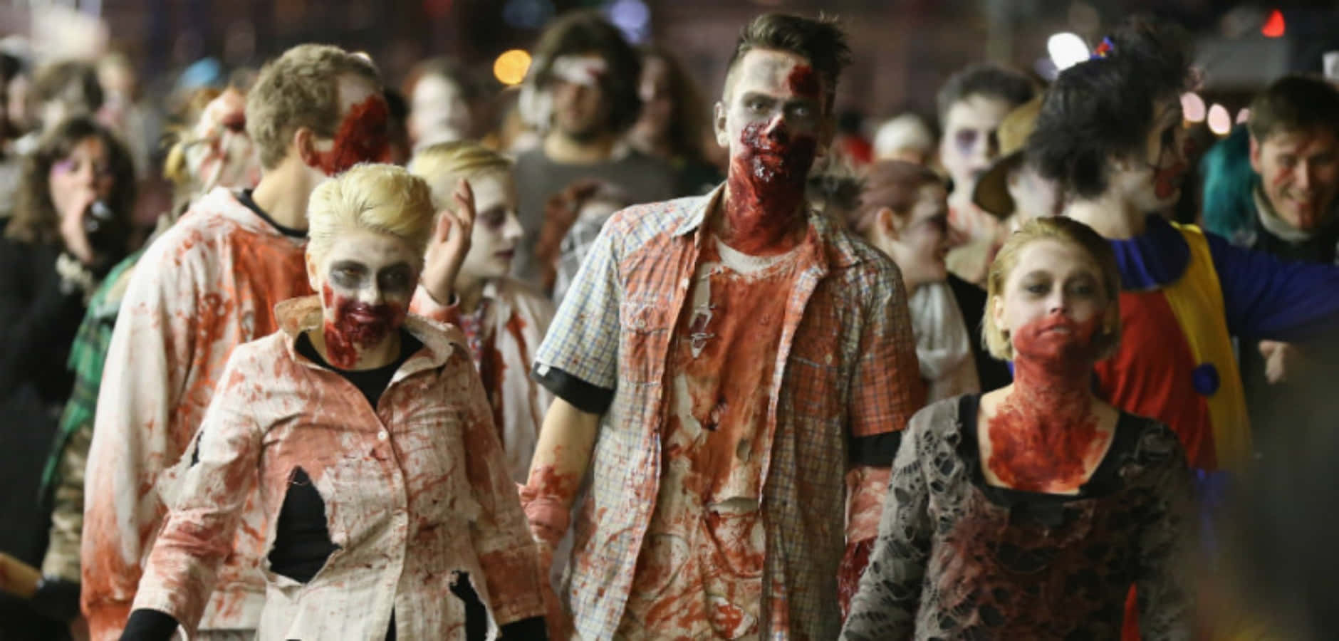 zombies 桌布 壁紙 — 一群穿著恐怖殭屍服裝、沾滿假血的人，在夜間的城市街道上行進。