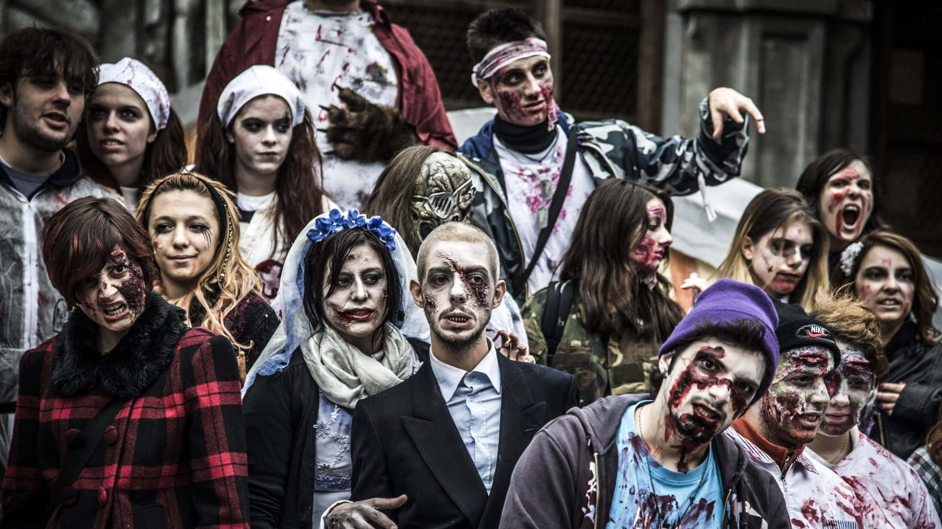 Zombie Costumes 桌布 壁紙 — 一群穿著恐怖殭屍服裝、滿臉鮮血、衣服破爛的人們在城市環境中拍照留念。