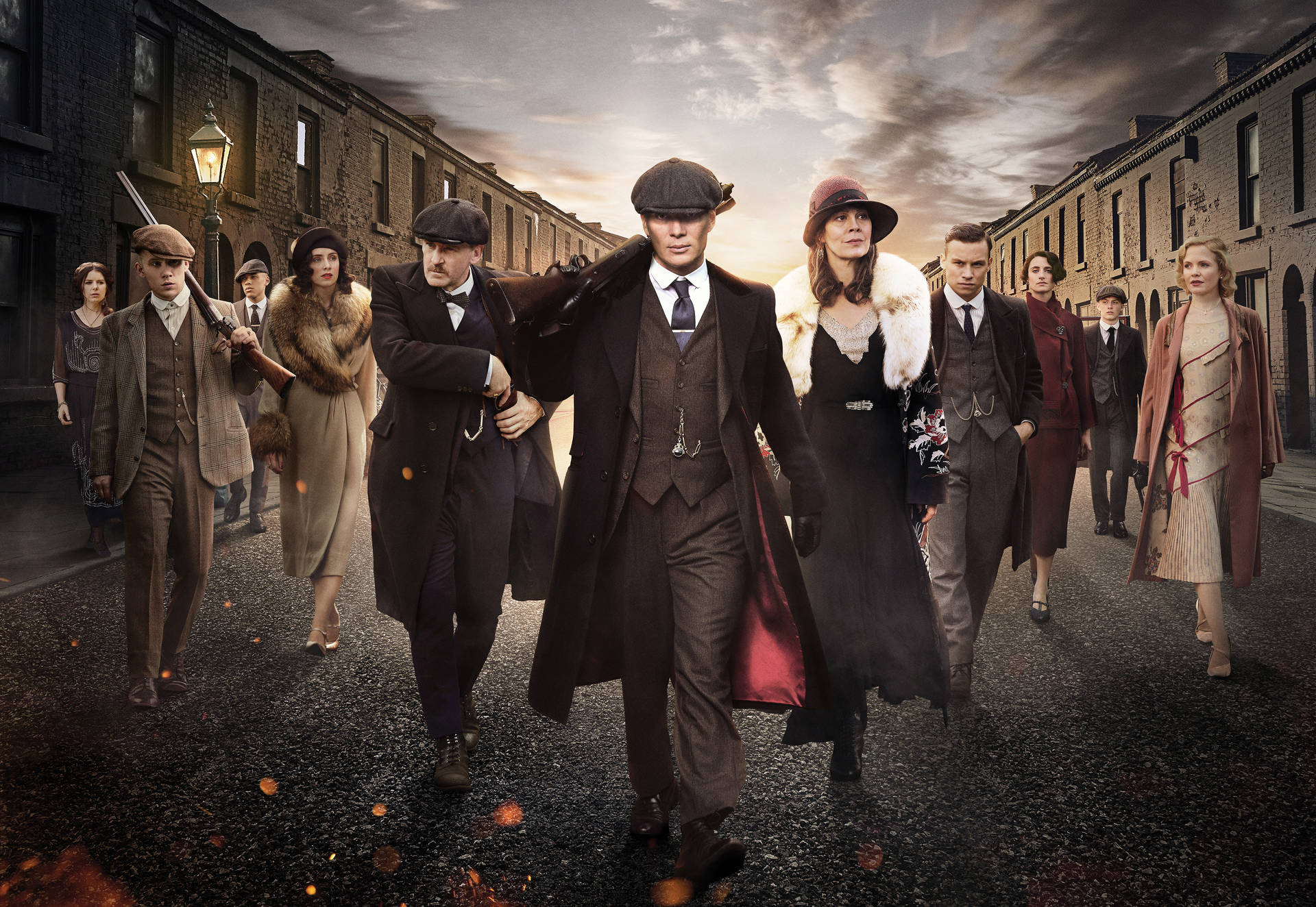 一群穿著1920年代服裝的人在黃昏時分沿著磚街行走。 — Peaky Blinders 壁紙