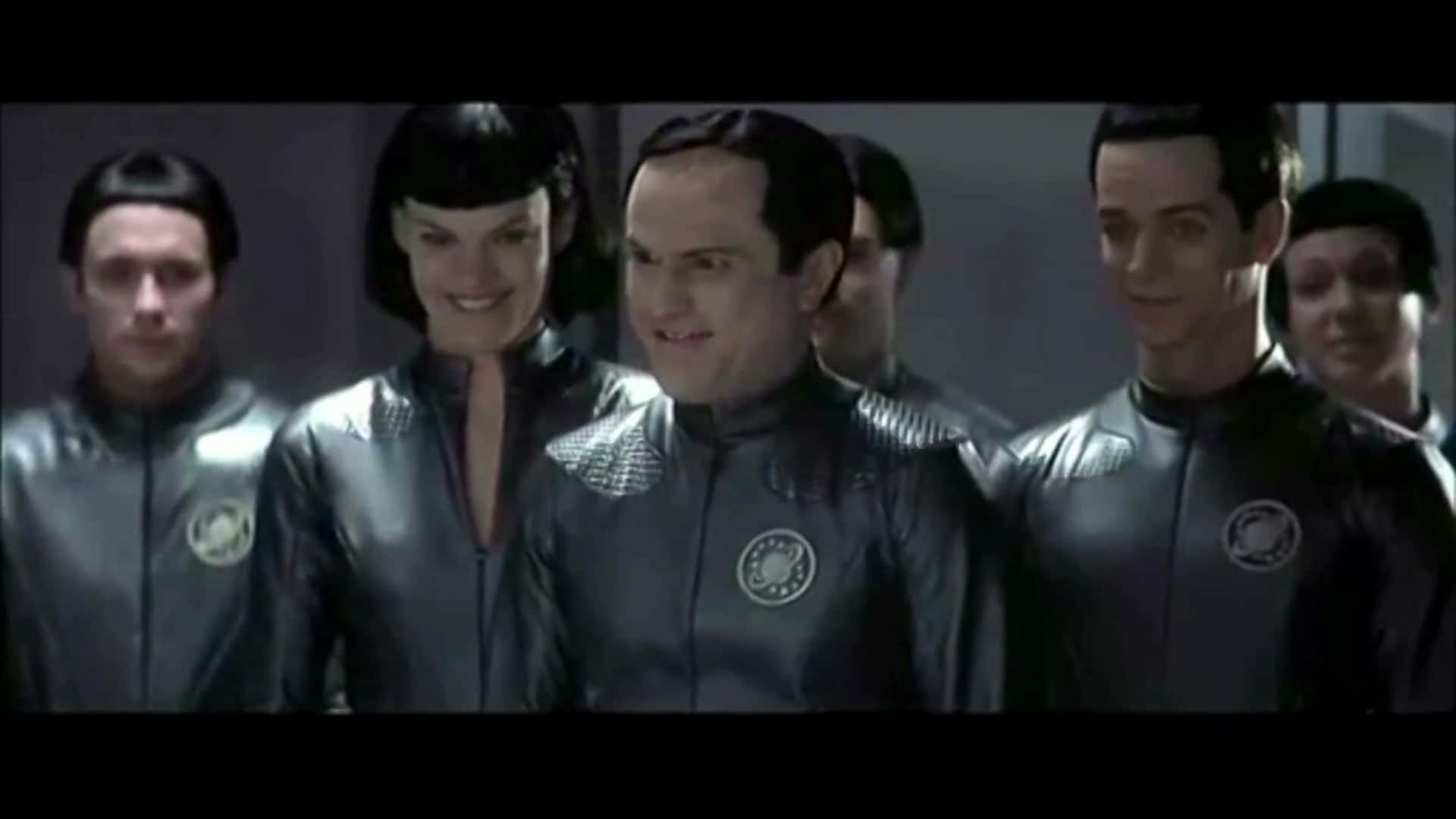 Galaxy Quest 桌布 壁紙 — 一群穿著時尚黑色制服的人，表情嚴肅地站在燈光昏暗的未來主義走廊中。