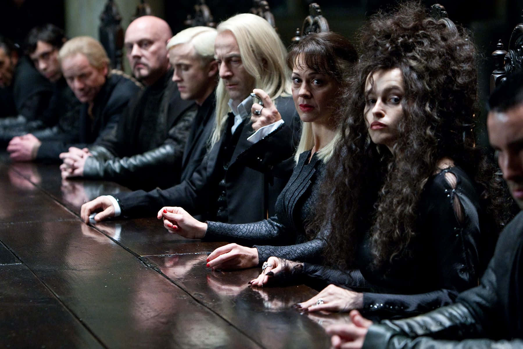 Death Eaters 桌布 壁紙 — 一群穿著深色衣服的角色莊嚴地坐在一張長長的拋光桌子旁，房間光線昏暗，風格哥德式。