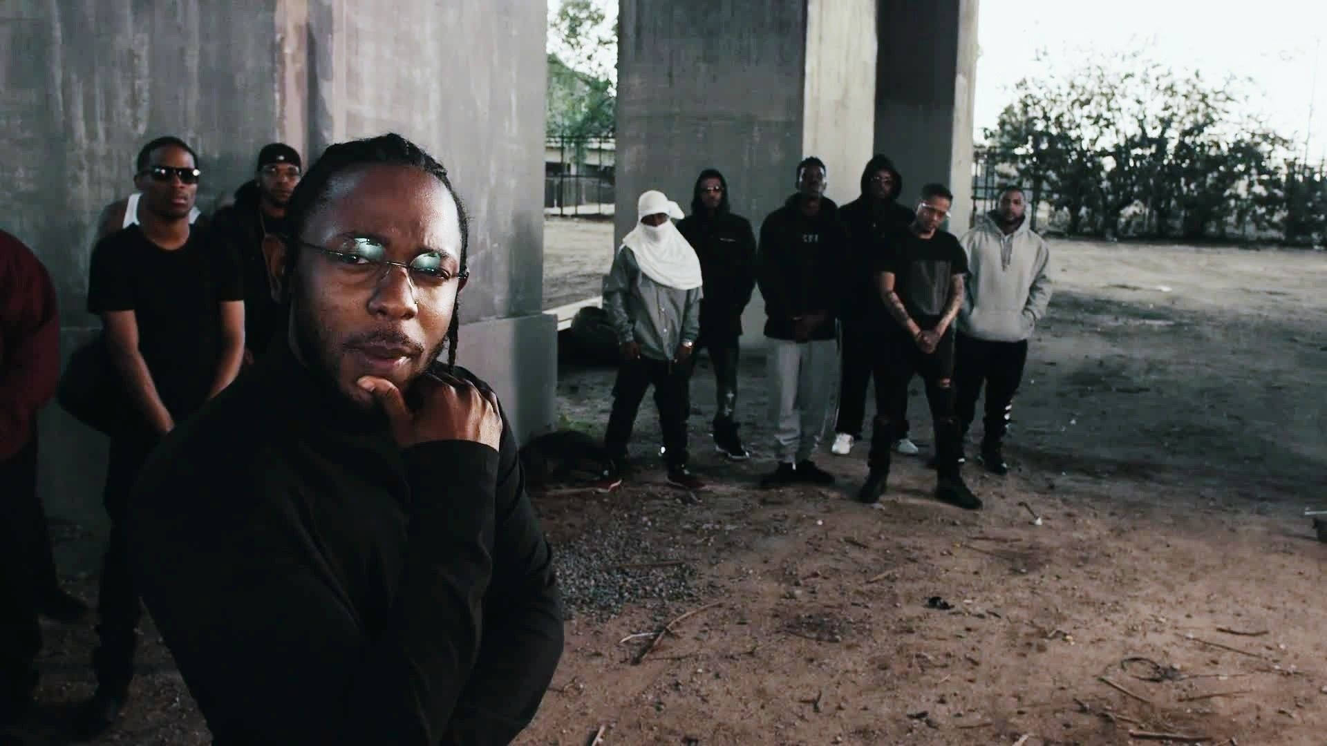 Kendrick 桌布 壁紙 — 一群穿著深色都市服裝的男子站在粗糙戶外環境的混凝土柱下。