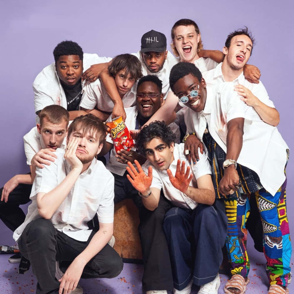 Brockhampton 桌布 壁紙 — 一群穿著白襯衫的多元年輕男性在紫色背景前頑皮地擺姿勢，其中一人拿著一袋薯片，另一人的手染成橙色。