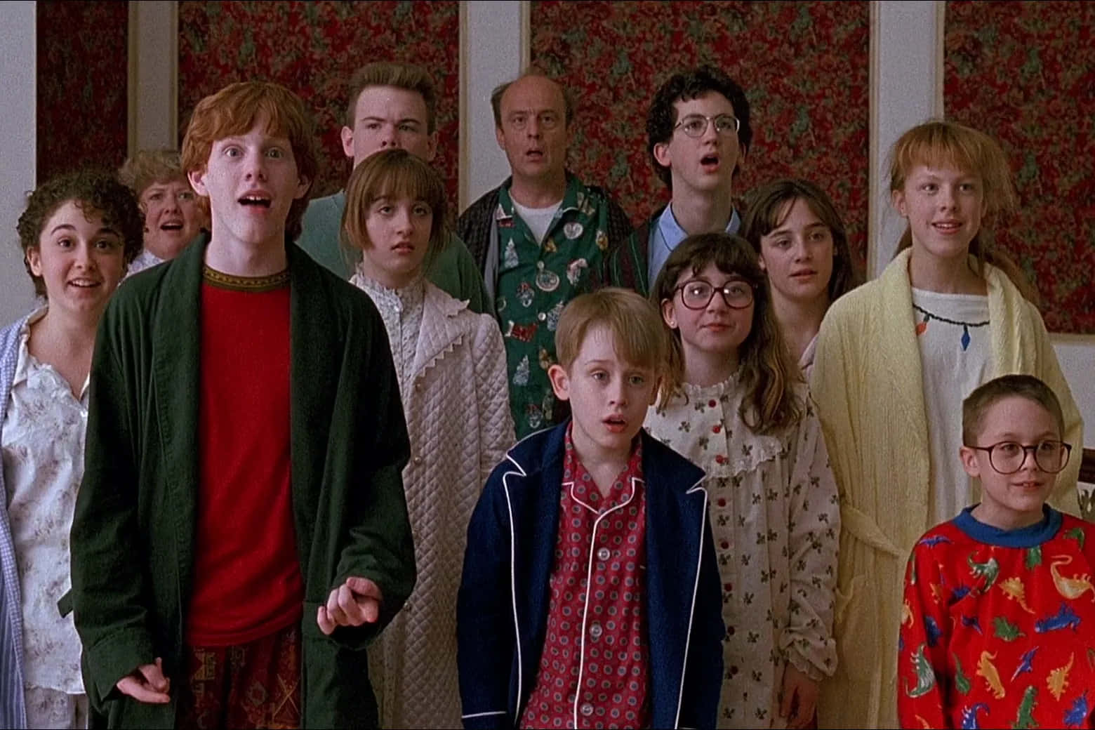 Home Alone 桌布 壁紙 — 一群穿著睡衣的兒童和成人，在一個有花卉壁紙的房間裡，震驚或有趣地凝視著。