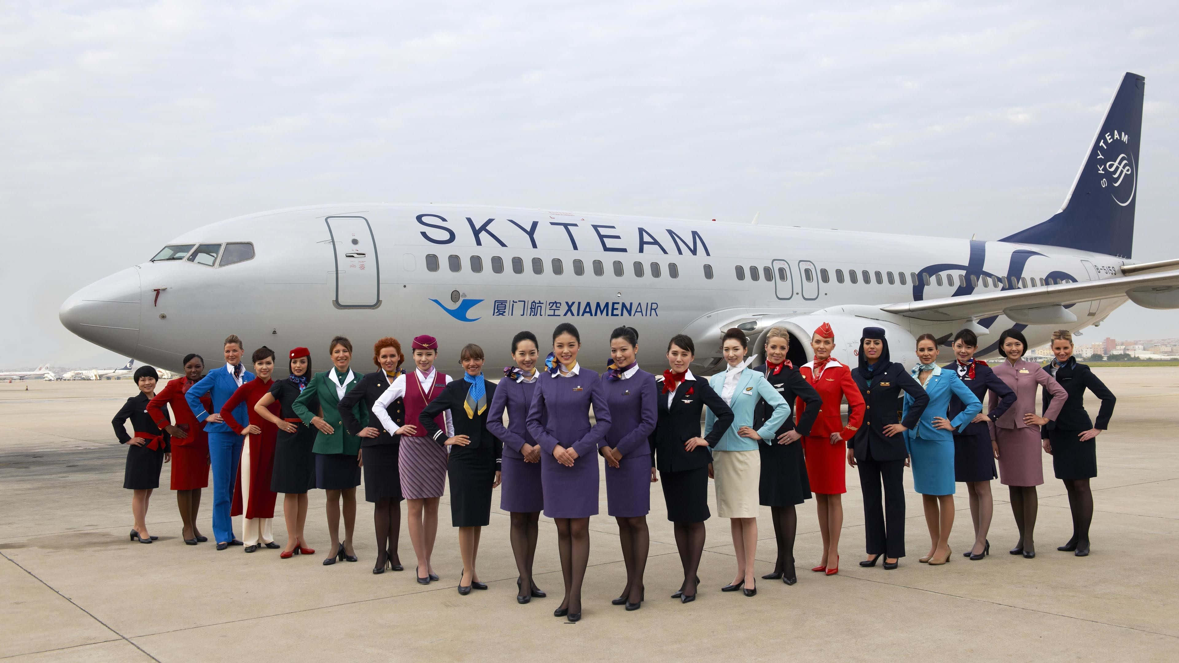 Flight Attendant 桌布 壁紙 — 一群穿著色彩繽紛制服的空中服務員在機場停機坪上，自信地在天合聯盟廈門航空飛機前擺姿勢。