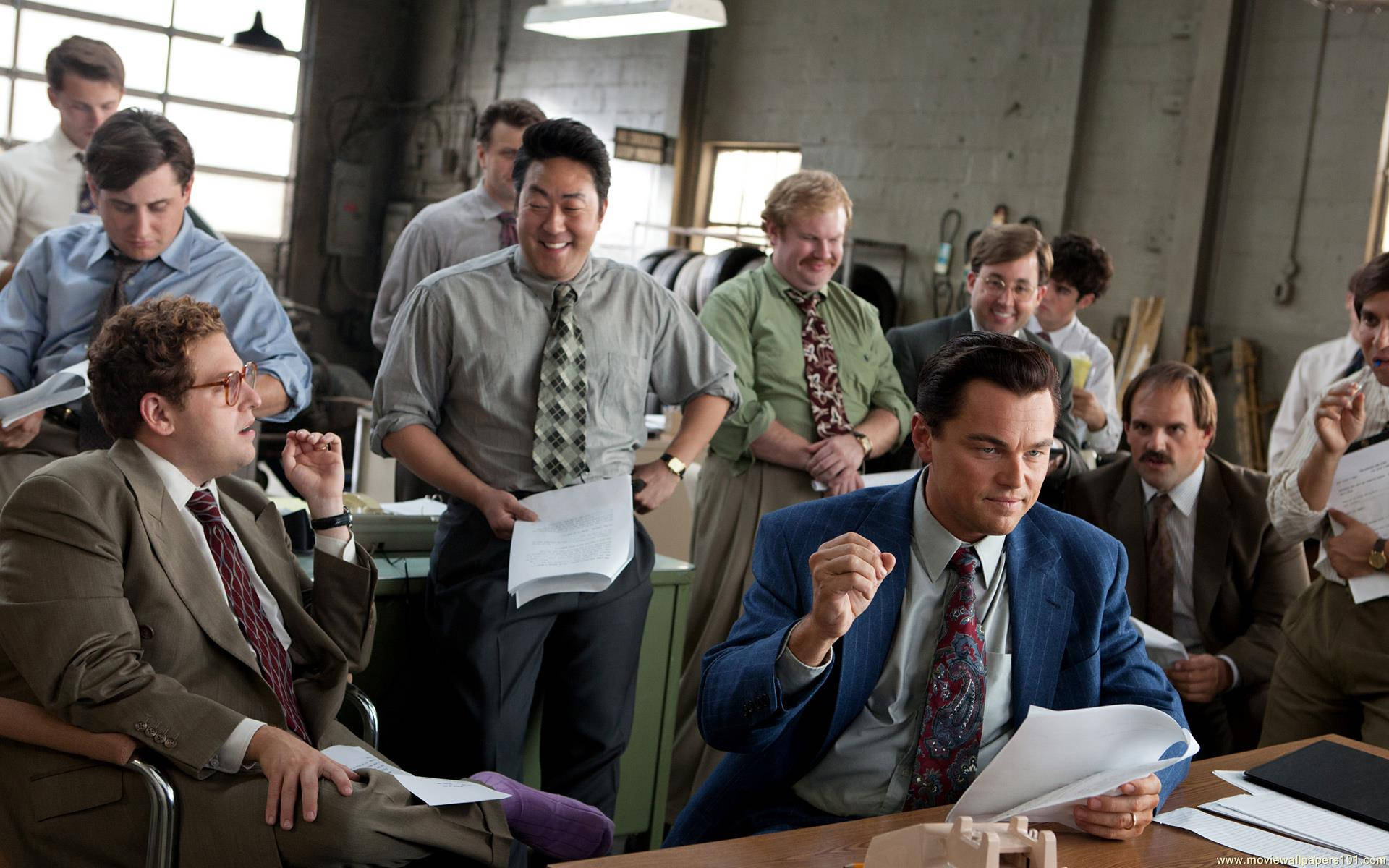 Wolf Of Wall Street 桌布 壁紙 — 一群穿著西裝打領帶的男人在雜亂的工業辦公室裡大笑並生動地比手畫腳。