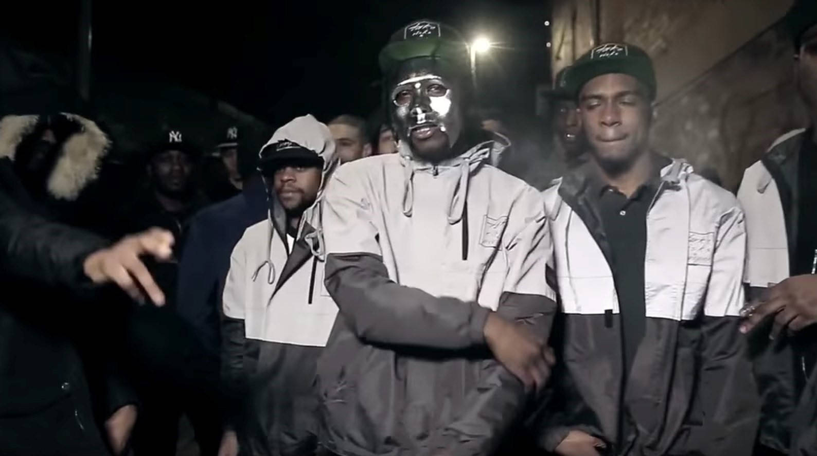 Rappers 桌布 壁紙 — 一群穿著連帽衫和帽子的男人在夜晚站在刺眼的路燈下，其中一人戴著反光的銀色面具。
