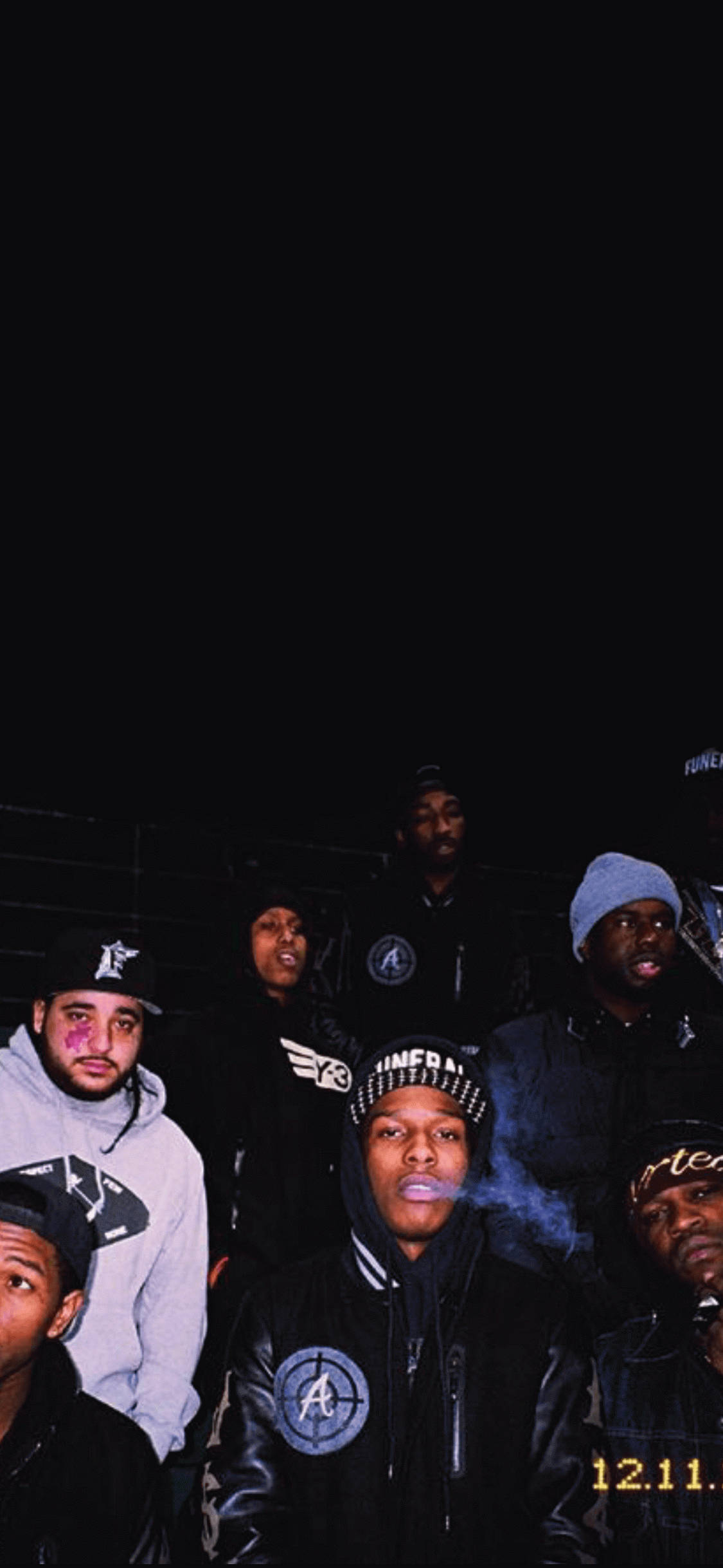 90s Rapper 桌布 壁紙 — 一群穿著連帽衫和毛線帽的年輕男子在夜間擺姿勢，其中一人口中冒煙，背景漆黑。