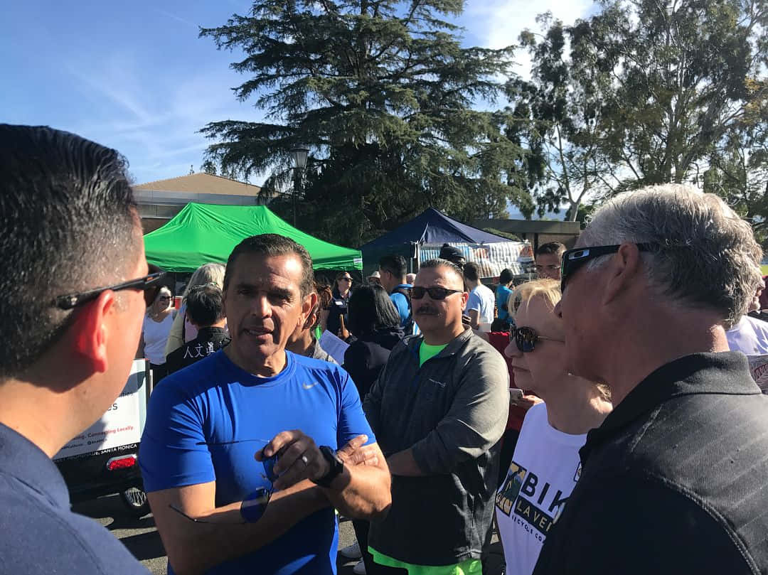 政治 桌布 壁紙 — 一群穿著運動服的人聚集在戶外，在明亮的陽光下，靠近活動帳篷和樹木。