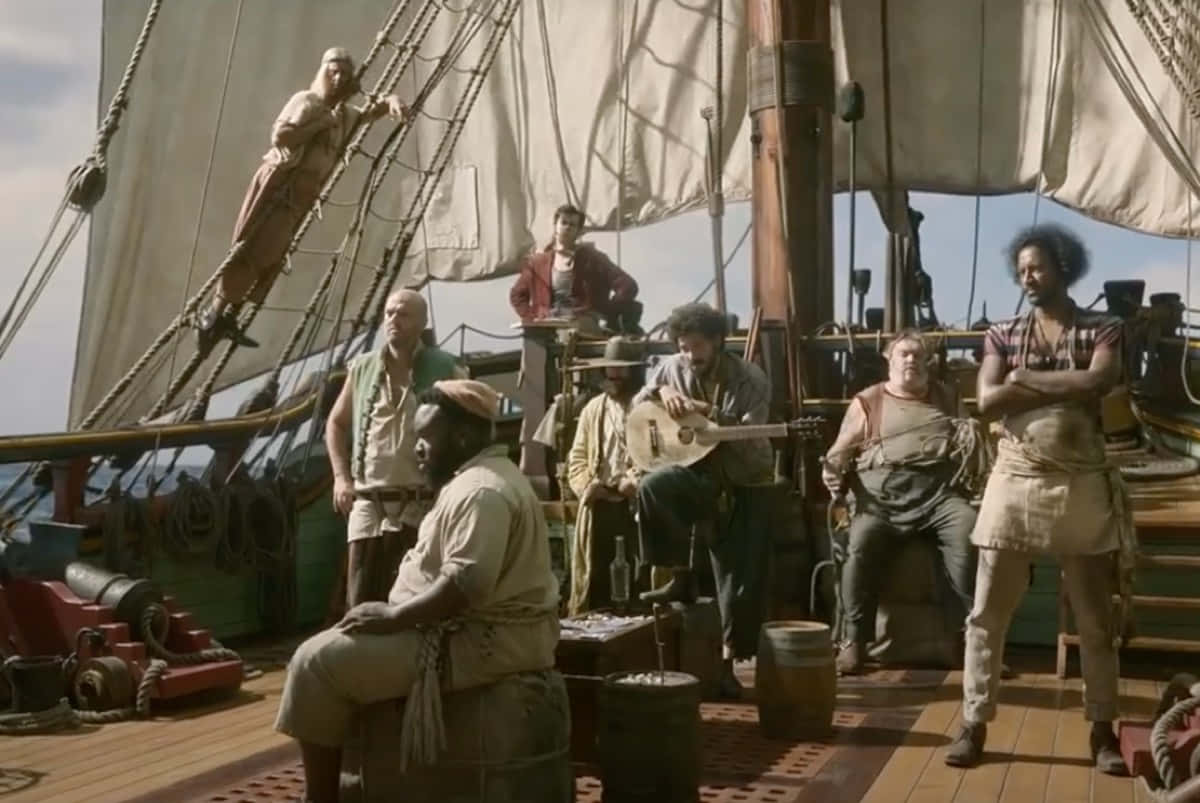 Pirate 桌布 壁紙 — 一群粗獷的海盜在陽光明媚的甲板上放鬆，一艘高桅帆船揚起風帆，大炮清晰可見。