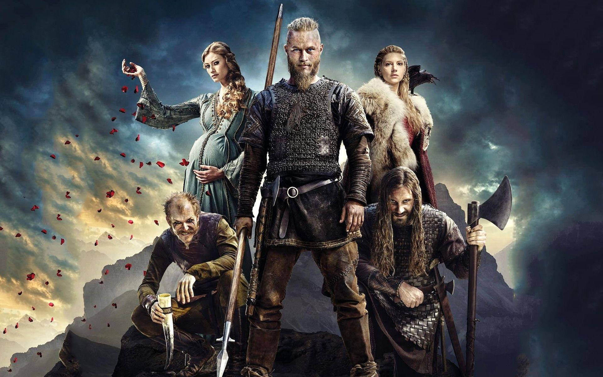 Vikings 桌布 壁紙 — 一群維京戰士和女性站在岩石峭壁上，暴風雨的天空下，紅色花瓣在他們周圍飄落。