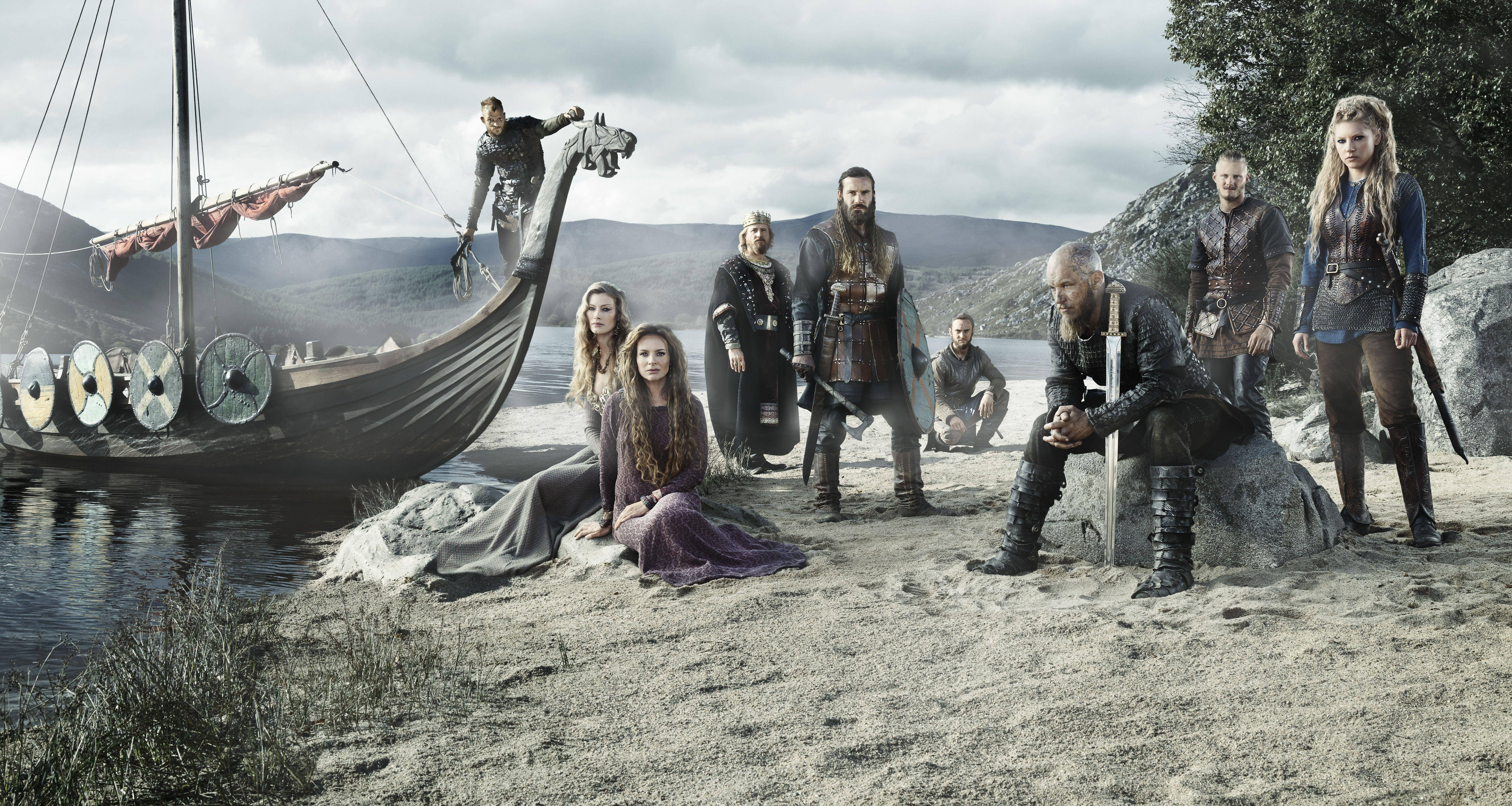Vikings 桌布 壁紙 — 一群維京船員站在他們的長船旁，背景是霧氣瀰漫的海岸線和山脈。