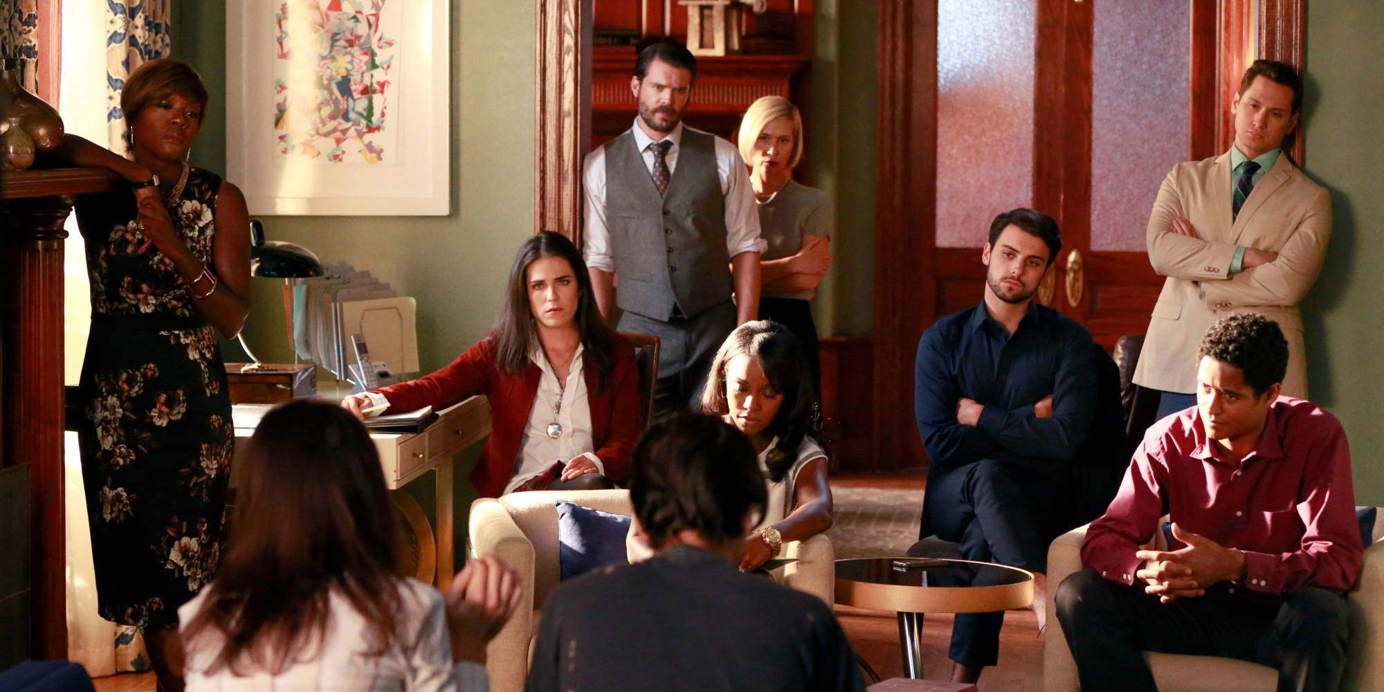 How To Get Away With Murder 桌布 壁紙 — 一群緊張的人在一間帶有木鑲板和復古裝飾的正式客廳中，專注地凝視著一個背對鏡頭坐著的人。