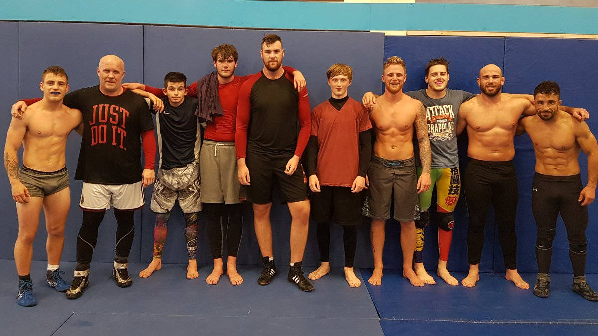 UFC 桌布 壁紙 — 一群肌肉發達的男子穿著摔角裝備，在藍色墊子上靠著軟墊牆壁一起擺姿勢。
