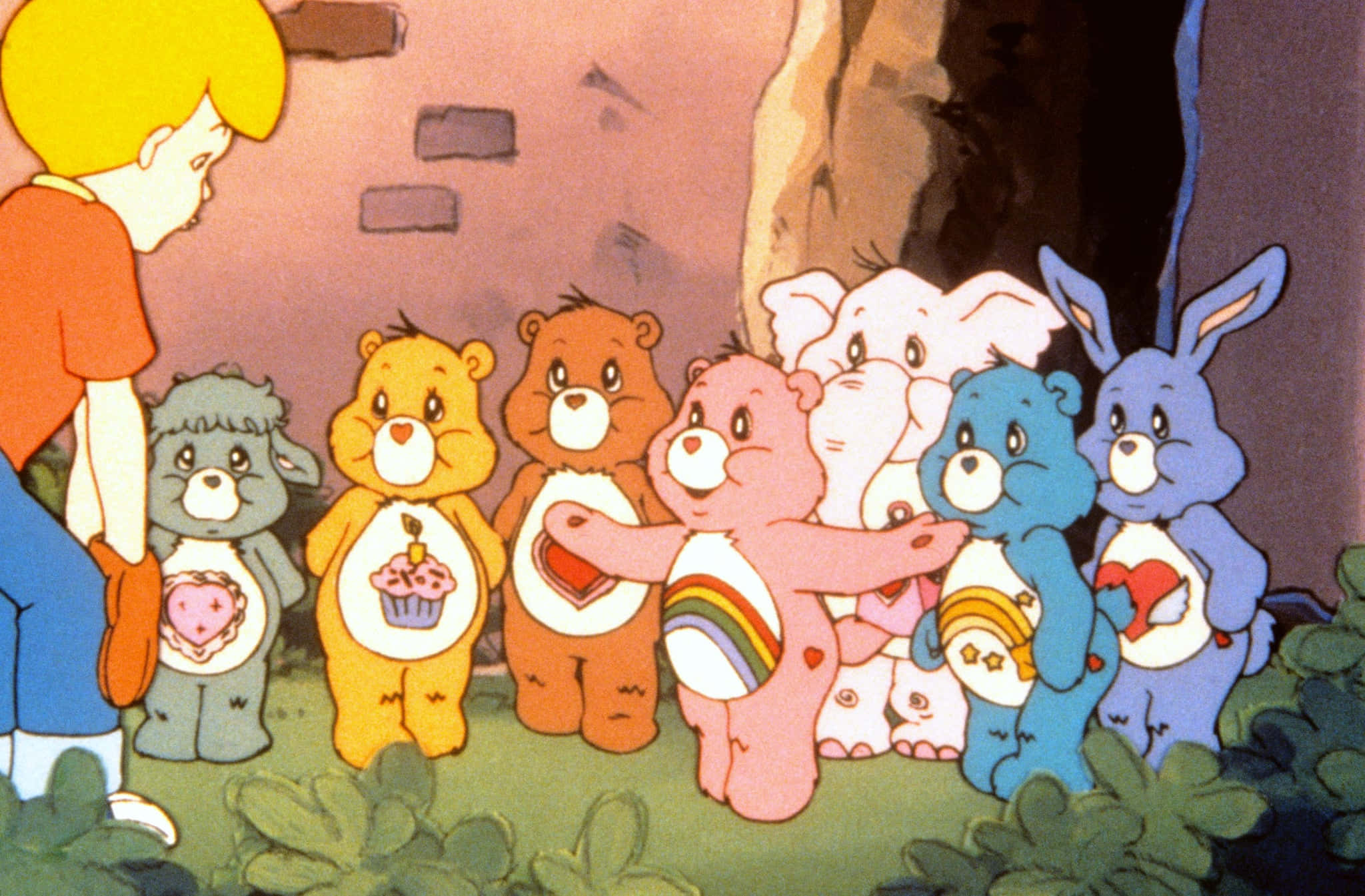 彩虹熊 桌布 壁紙 — 一群色彩繽紛的Care Bears，肚子上有心形圖案徽章，聚集在洞穴入口附近的森林空地。
