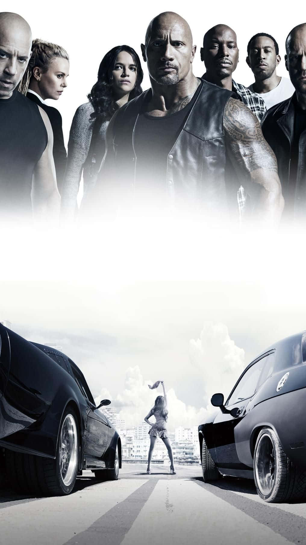 Fast And Furious Desktop 桌布 壁紙 — 一群表情強烈的演員站在一位在兩輛黑色肌肉車之間跳舞的女人上方，背景是城市街道。