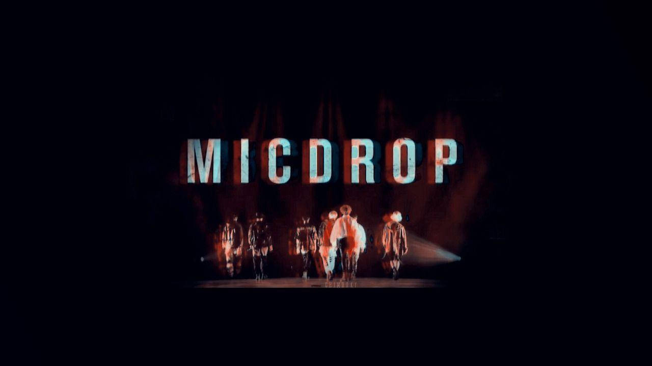 BTS 筆電 桌布 壁紙 — 一群表演者站在黑暗的舞台上，下方是發光的「MICDROP」標誌，伴隨著戲劇性的紅色和藍色燈光。