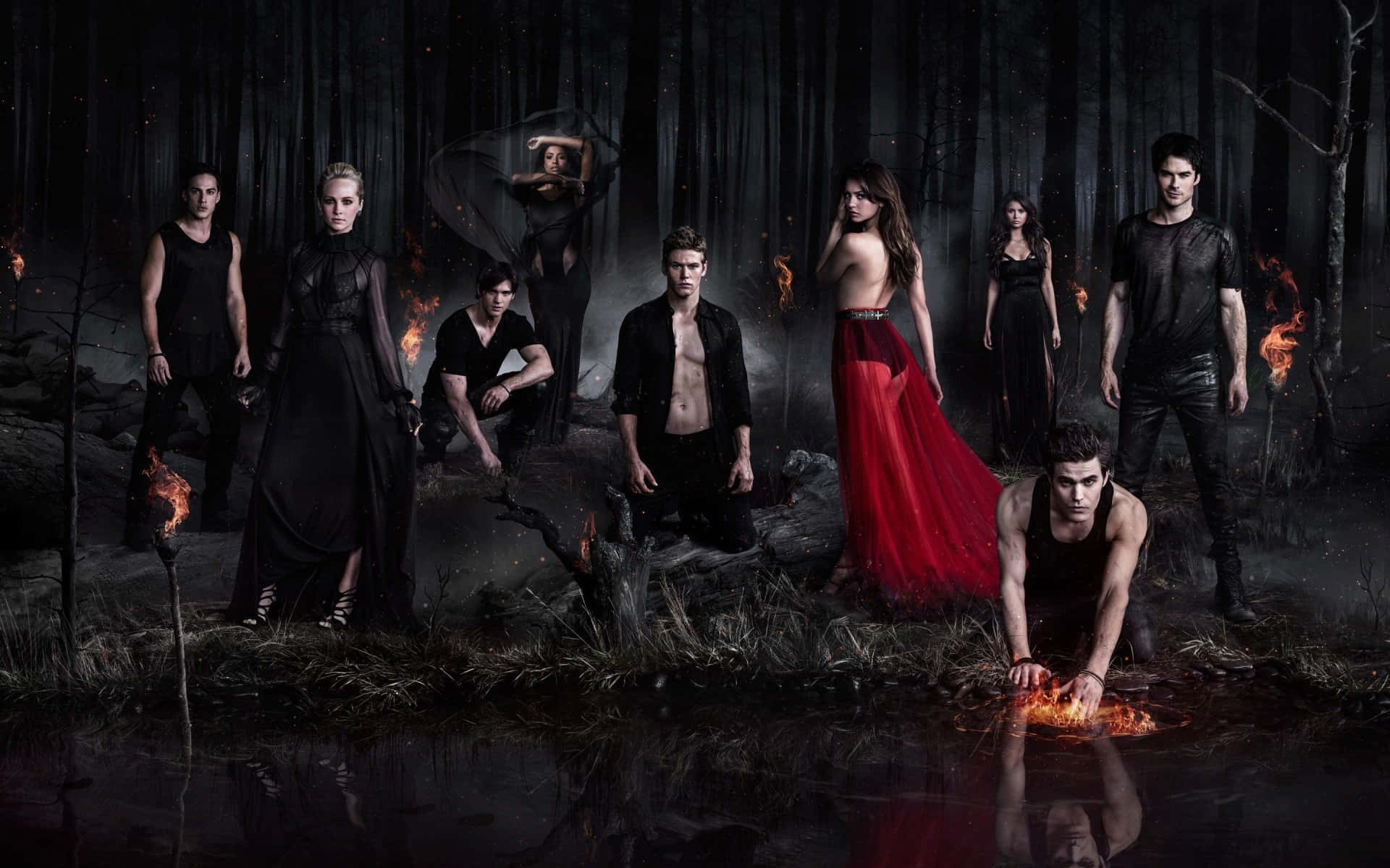 Vampire Diaries Desktop 桌布 壁紙 — 一群角色在黑暗的森林中，有火和水，其中一位穿紅色連衣裙的女性在其他人穿黑色中脫穎而出。