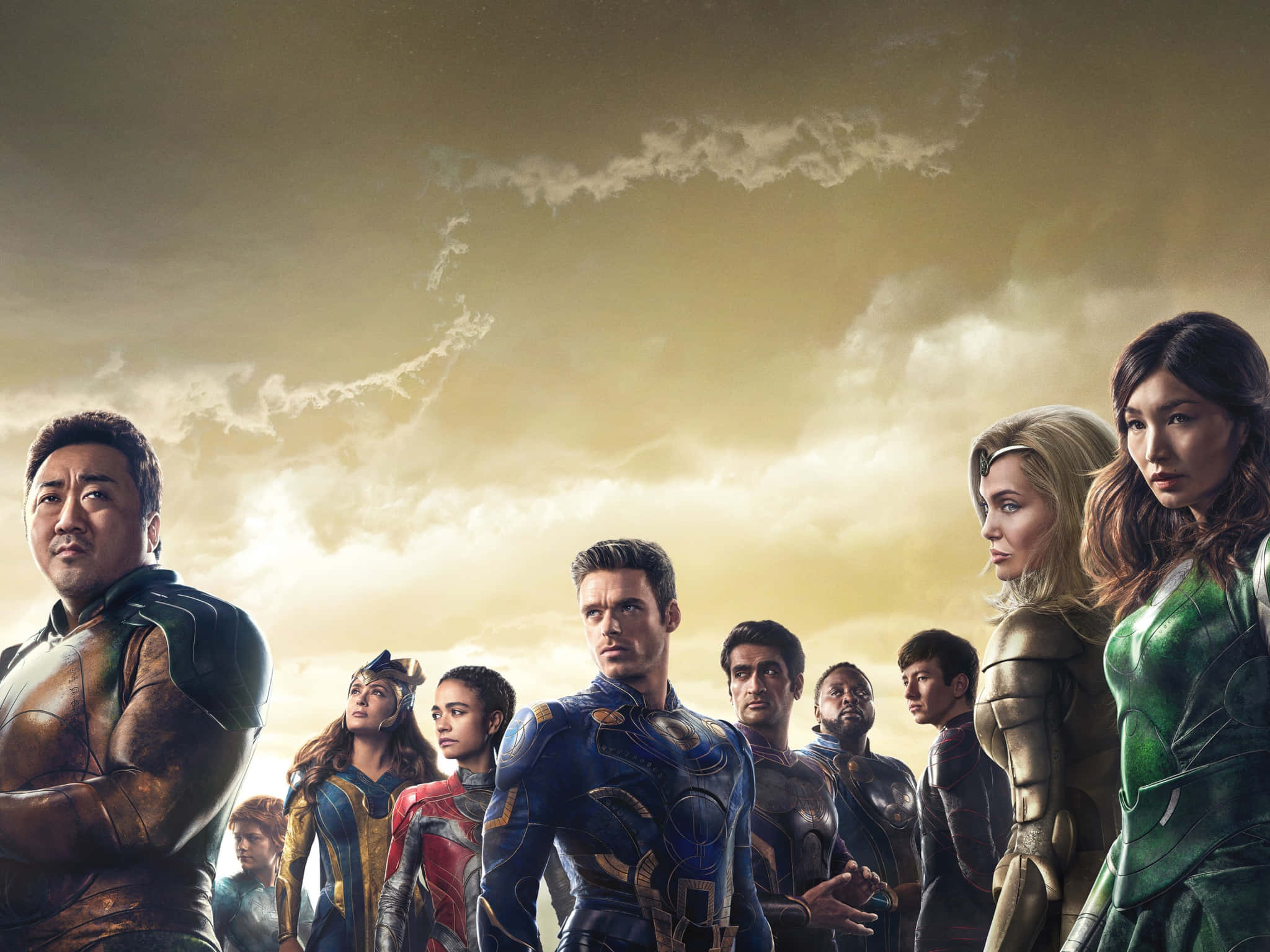 Eternals Movie 桌布 壁紙 — 一群身穿未來裝甲的超級英雄，在金色天空和戲劇性雲彩的映襯下堅定站立。