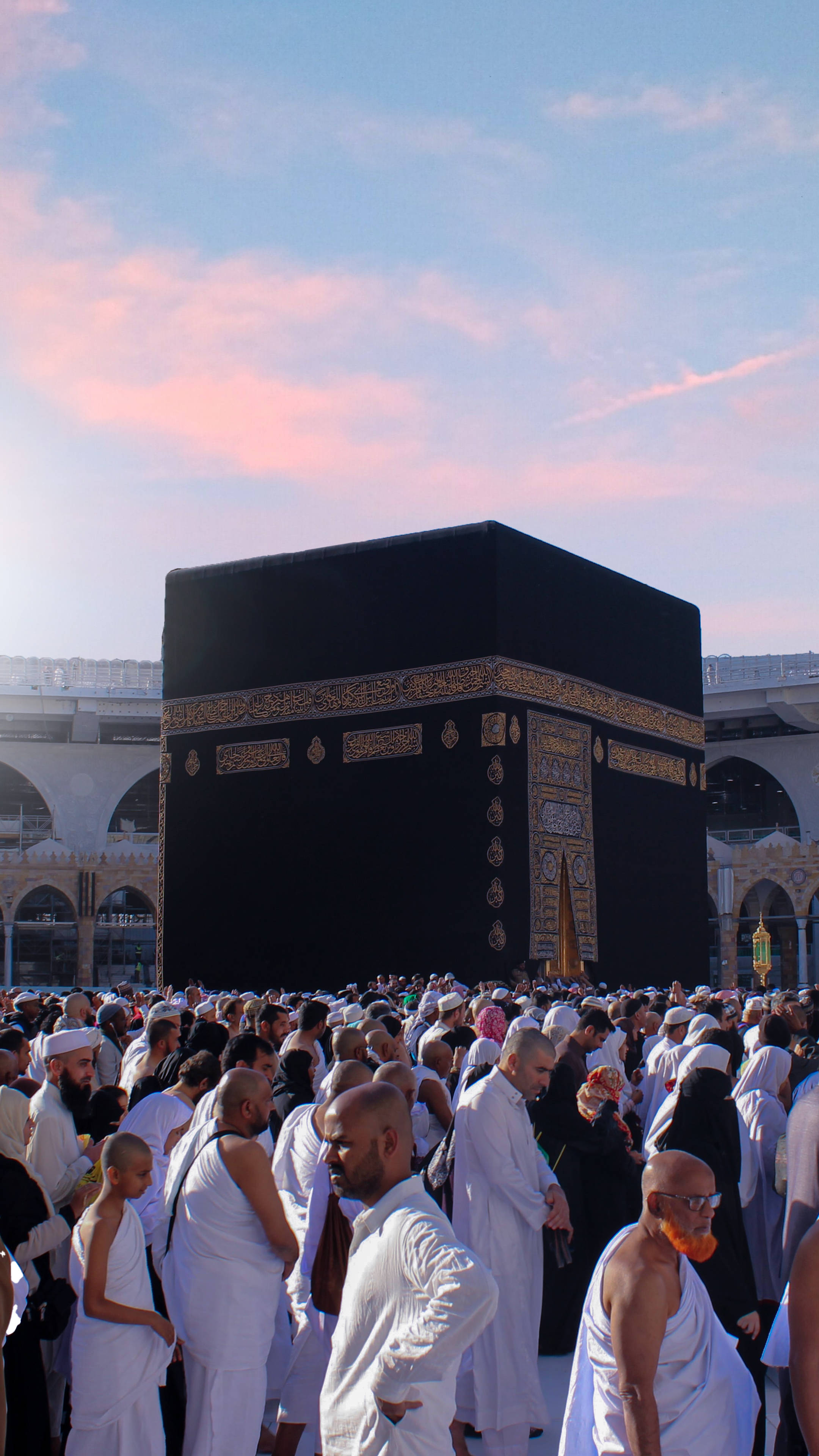 muslim 桌布 壁紙 — 一群身穿白色朝聖服（伊赫拉姆）的朝聖者，在柔和的粉紅與藍色暮色天空下，繞行黑色卡巴天房。