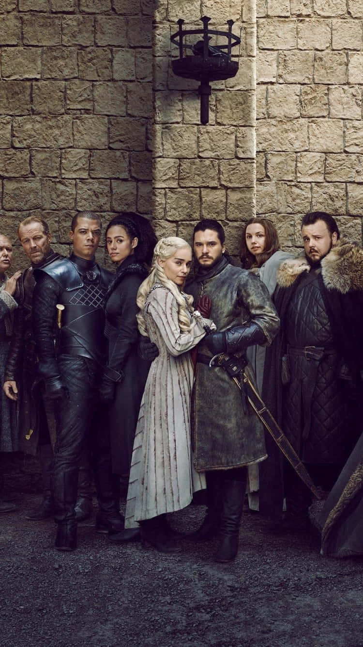Game Of Thrones iPhone 桌布 壁紙 — 一群身穿盔甲的中世紀人物在掛著的燈籠下，莊嚴地站在粗糙的石城堡牆前。