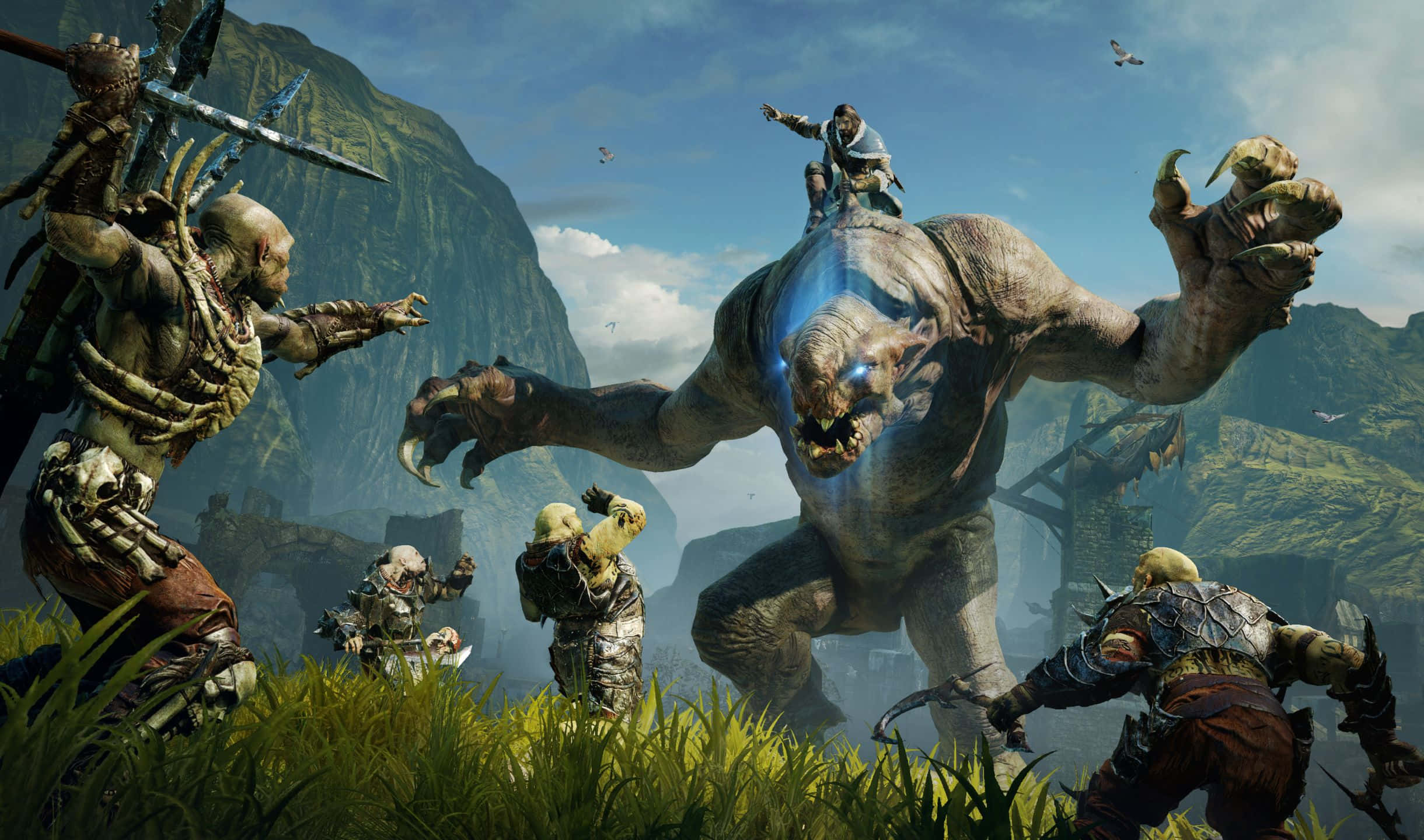2440x1440 Shadow Of Mordor 桌布 壁紙 — 一群身穿盔甲的戰士在青翠的山谷中，在明亮的藍天下與一隻巨大的發光眼睛的野獸戰鬥。