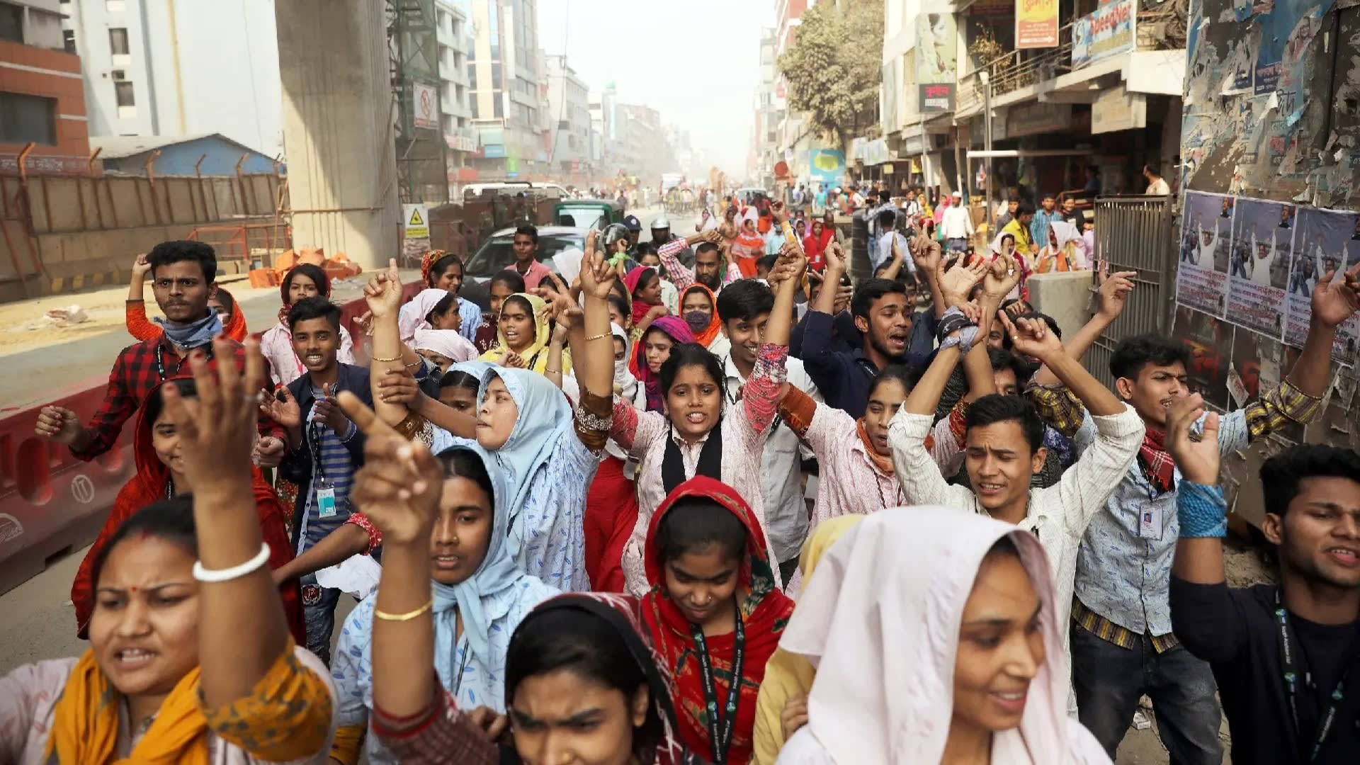 Bangladesh 桌布 壁紙 — 一群身穿色彩繽紛傳統服飾的人群，在佈滿建築物和海報的繁忙城市街道上齊聲舉手。