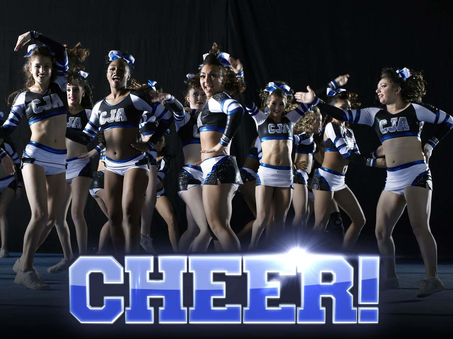 Cheer 桌布 壁紙 — 一群身穿藍白制服、充滿活力的啦啦隊員在黑色背景前擺出充滿活力的姿勢，背景上有一個發光的「CHEER!」圖案。
